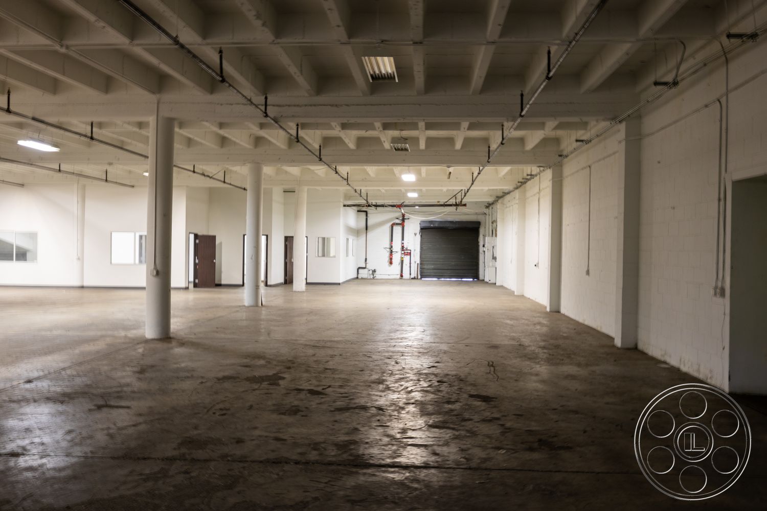 Warehouse 61 - neutral color palette, open floor plan, concrete block walls, steel support columns, commercial building interior, functional workspace layout, exposed concrete floors, painted drywall interior, tall industrial ceiling, large warehouse windows, metal fire sprinkler system, modern minimalist space, urban industrial style, unfinished concrete aesthetic, flexible usage space, commercial lighting fixtures, rolldoor access, wide open area, concrete ceiling beams, interior industrial design