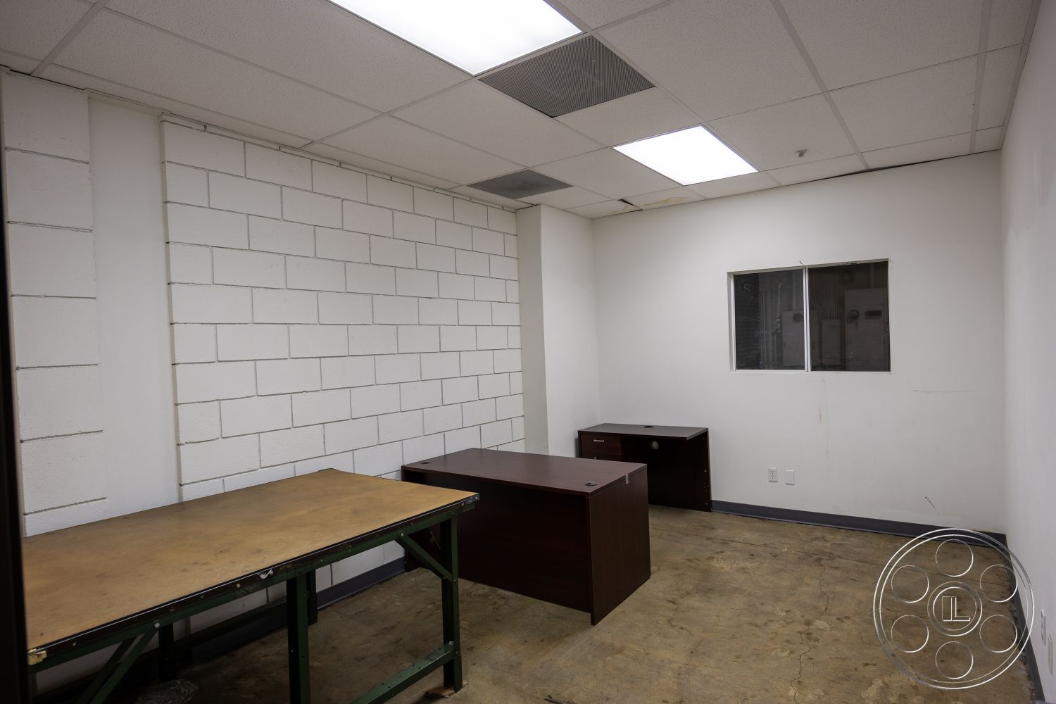 Warehouse 61 - minimalist design, concrete floor, white painted walls, drop ceiling tiles, commercial office space, exposed concrete block walls, steel frame desk with wooden finish, single window, unfinished office environment