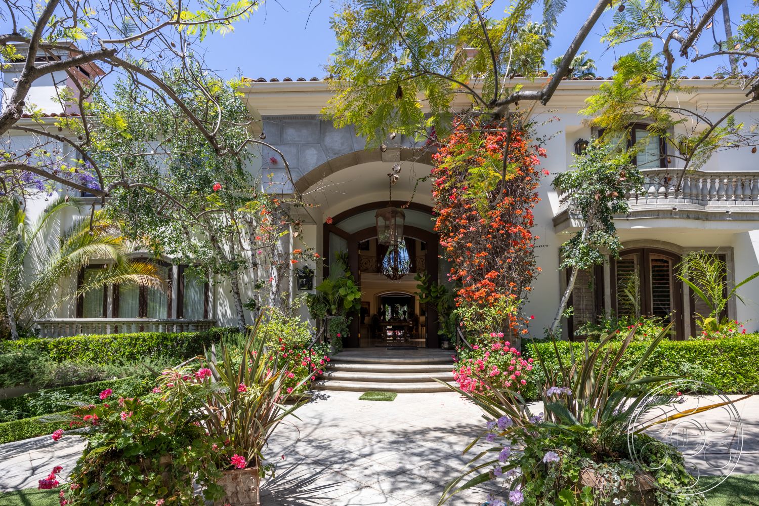 Medit 165 - exterior, stucco walls, arched doorways, modern chandelier, stone feature wall, decorative wrought iron railing, stone patio flooring, landscaped garden with tropical plants, curved entrance steps, flush wood panel doors, paved walkway with decorative tiles, balcony with decorative balustrades, lush flower beds, vaulted ceiling over entrance, mediterranean architectural style, surrounding garden setting