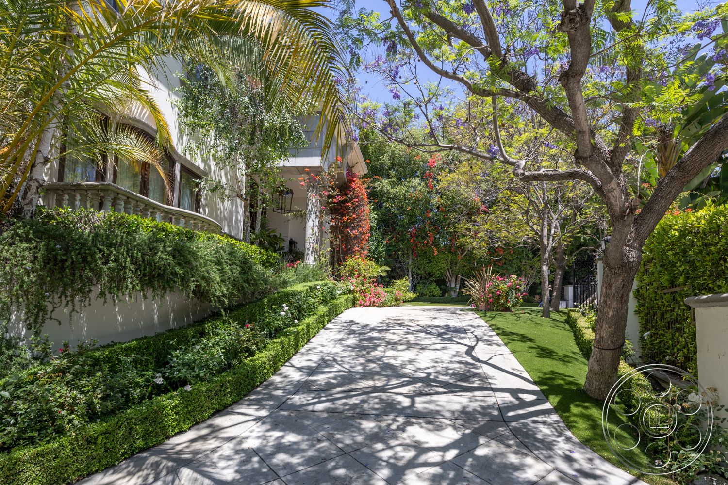 Medit 165 - landscaped garden, lush greenery, garden path, concrete driveway, curved driveway, colorful flower beds, sunlit exterior, hilltop location, modern residential architecture, two-story home, shaded patio area, urban garden setting, exterior stone feature wall, brick courtyard walls, exterior ornamental plants, textured concrete pavers, palms and tropical plants, ornate balcony railing, natural light accents, architectural decorative lanterns