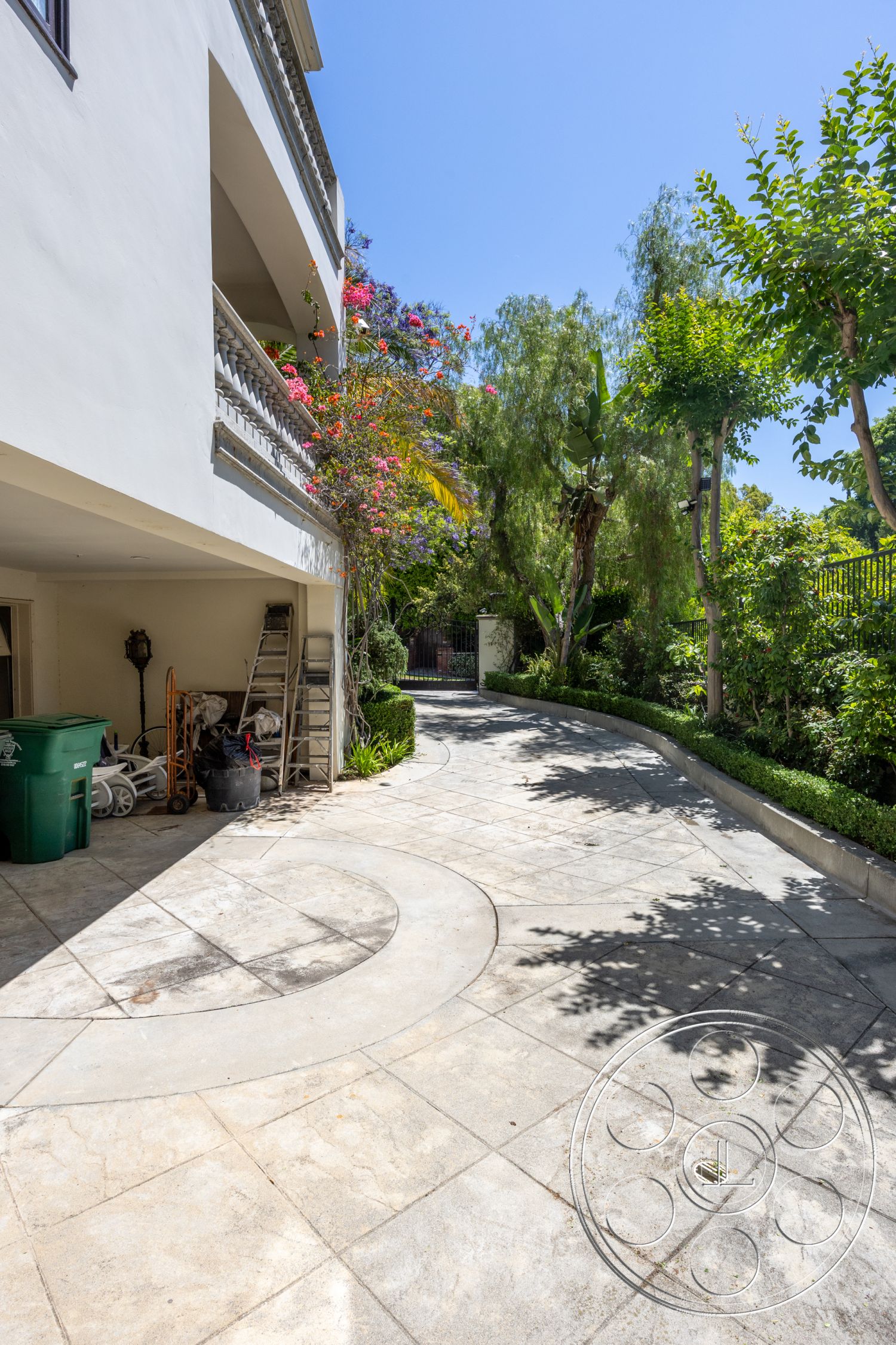 Medit 165 - concrete walkway, landscaped garden setting, stucco exterior walls, exterior concrete driveway, decorative wrought iron fence, sunny outdoor environment, curved concrete driveway, exposed aggregate concrete finish, surrounding tropical vegetation, stone garden border, attached garage access, slate accent stone, outdoor planter beds, second-story balcony railing, landscape lighting features