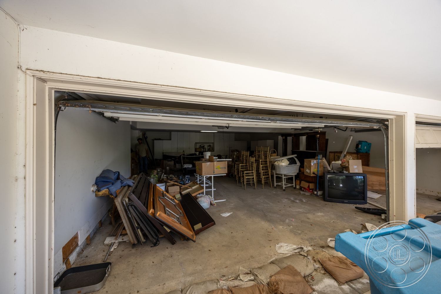 Medit 165 - unfinished ceiling, metal folding chairs, television display, painted drywall walls, concrete garage floor, stacked cardboard boxes, interior garage space, light wood paneling on walls, utility shelving units, cluttered storage area, modern garage door opening, various household items, cleaning supplies storage, horizontal wooden planks, direct garage access