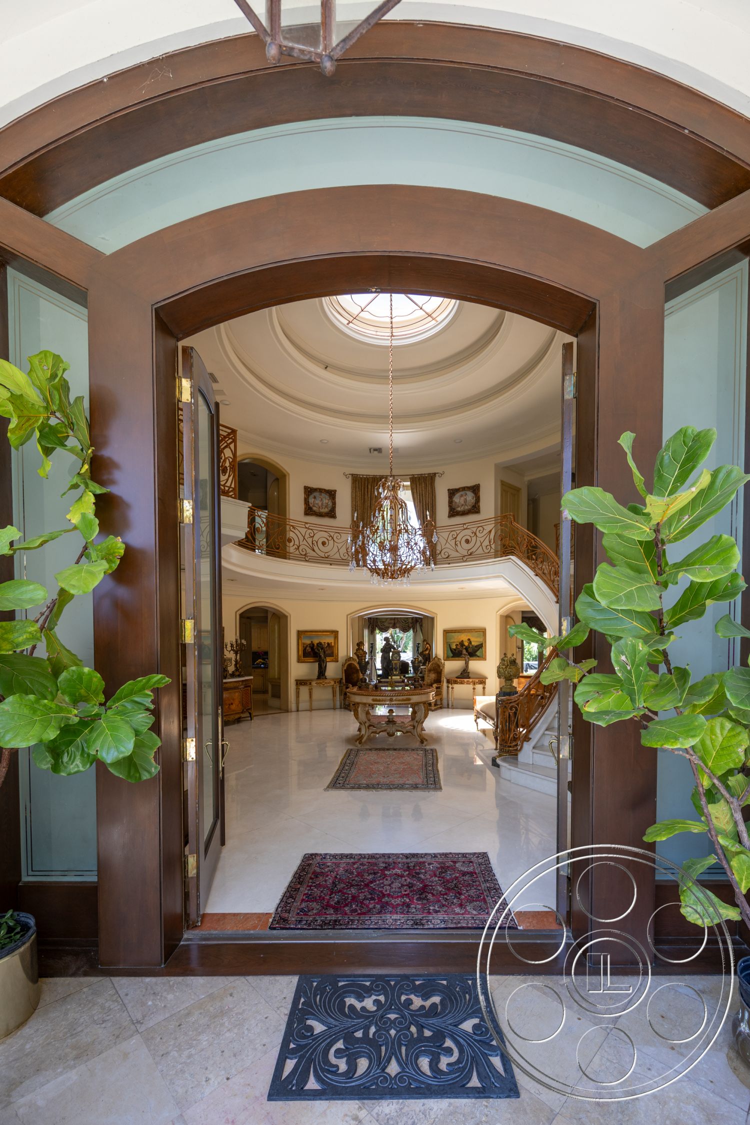 Medit 165 - open floor plan, decorative wall art, double front doors, curved staircase, wooden handrails, exposed wood door frame, marble foyer flooring, circular entryway, decorative wrought iron welcome mat, coffered ceiling with chandelier, interior soft color painted walls, large round skylight, ornate wall moldings, elegant furniture arrangement, floral indoor plants, luxurious rug accents, bright, natural lighting, southern exposure windows, formal living space, transitional architectural style