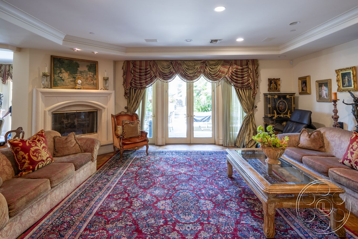 Medit 165 - high ceilings, wood flooring, decorative candle holders, decorative crown molding, outdoor view, ornate area rug, traditional furniture, lush greenery outside, elegant drapery, interior living room, custom built-in cabinetry, cream painted walls, fireplace with stone surround, upholstered sofa with ornamental cushions, glass coffee table with wooden frame, classic wall art, antique-style accent chair