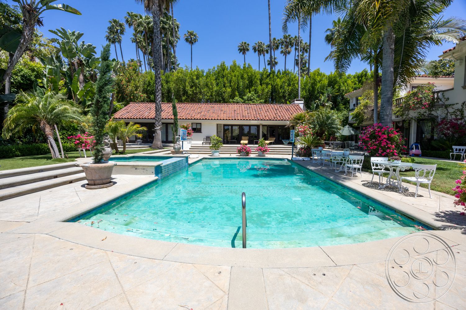 Medit 165 - exterior, glass sliding doors, rectangular swimming pool, outdoor dining area, terracotta roof tiles, open-air living space, lush tropical garden, concrete patio flooring, concrete pool border, stone deck, hardscape landscaping, palm trees surrounding pool area, white wrought iron patio furniture, flowering bougainvillea plants, multi-level deck with steps, urban oasis setting, sunlit, bright ambiance