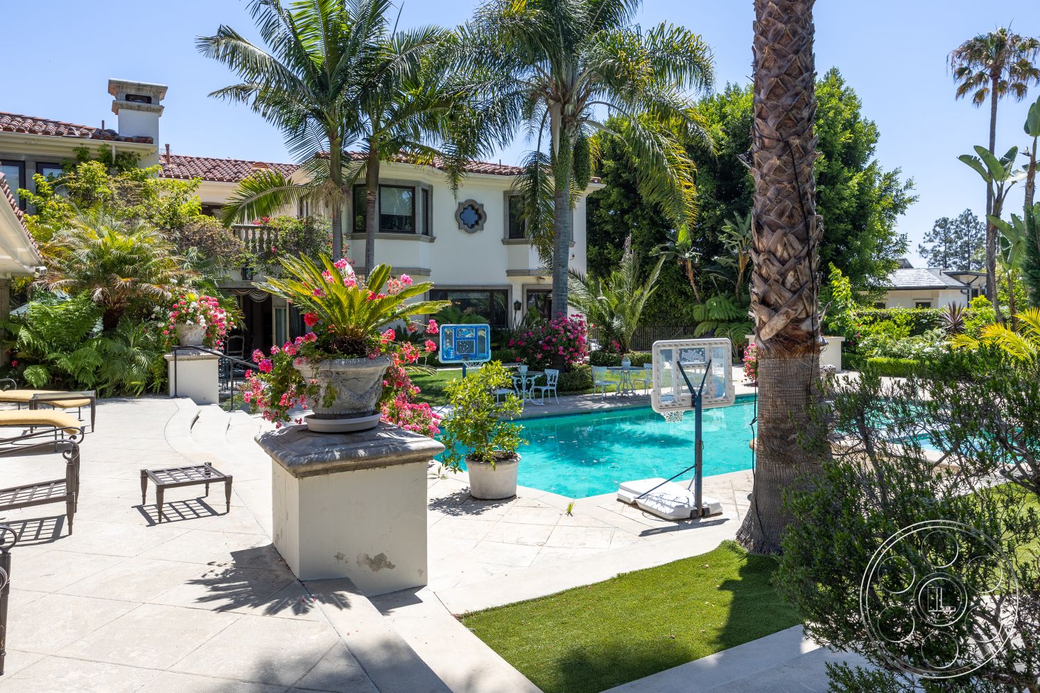 Medit 165 - exterior, palm trees, outdoor seating area, swimming pool, city skyline view, basketball hoop, vibrant greenery, rectangular pool, Mediterranean architectural style, landscaped garden area, concrete patio flooring, concrete pool border, lush tropical plants, sunny backyard setting, flower planters, iron patio furniture, stone garden pathway, decorative flower pots, courtyard home