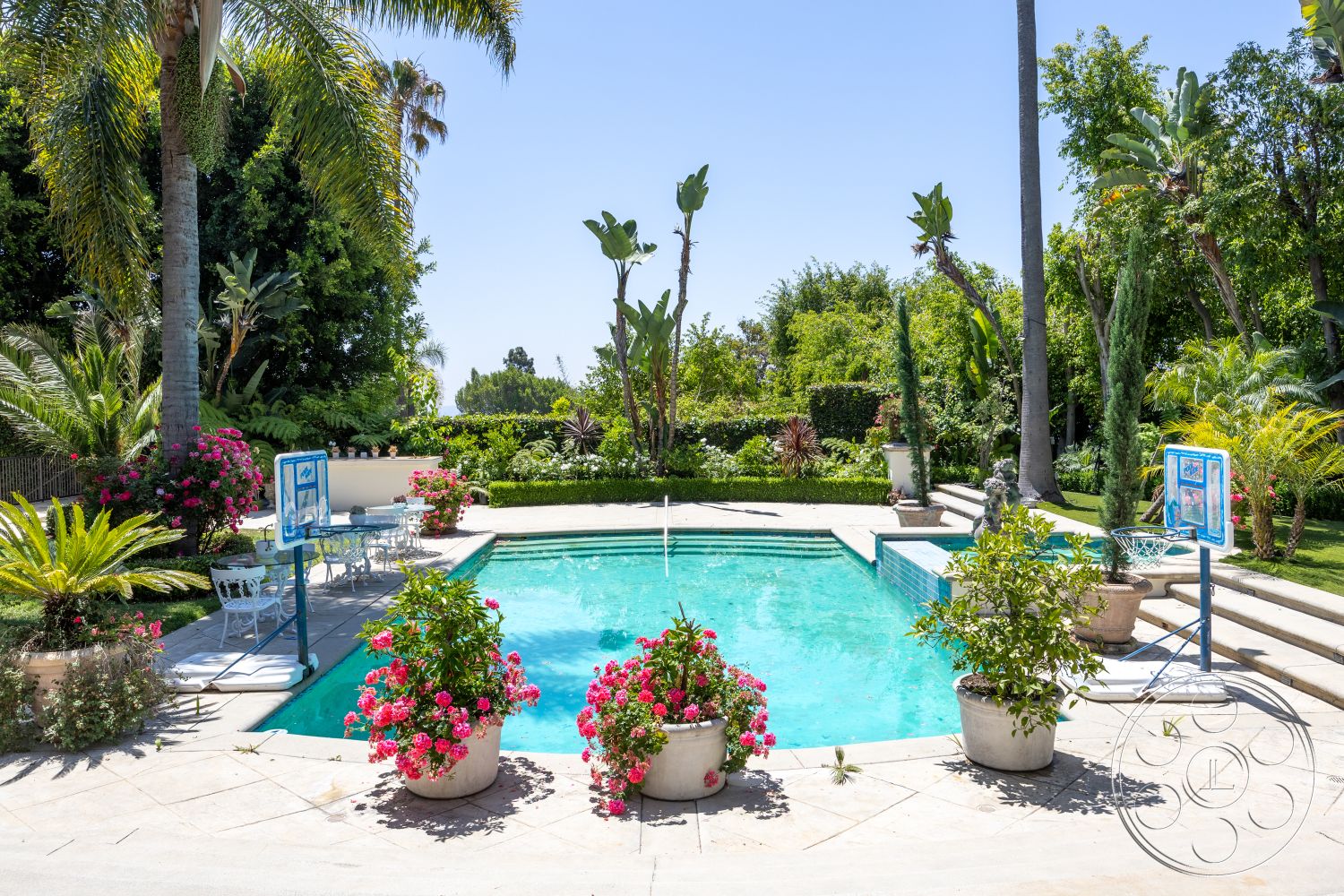 Medit 165 - exterior, landscaped garden, colorful flower pots, rectangular pool, poolside seating area, sunny outdoor space, decorative stone planters, stone patio flooring, concrete pool border, tropical plant surroundings, brick BBQ area, glass pool fencing, steel poolside loungers, white wrought iron furniture, hardscaped walkway, desert climate setting, private backyard oasis, palm tree accents, functional outdoor sports area