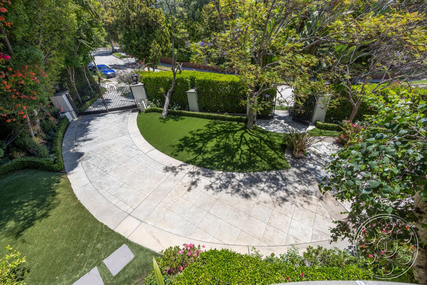 Medit 165 - urban setting, curved driveway, tropical landscaping, privacy hedges, outdoor lighting fixtures, textured concrete surface, landscaped garden area, lush green foliage, luxury home exterior, manicured grass lawn, decorative stone borders, stamped concrete driveway, exterior gated entrance, seasonal flowering plants, shadow patterns on driveway, brick entrance pillars, softscaped elements