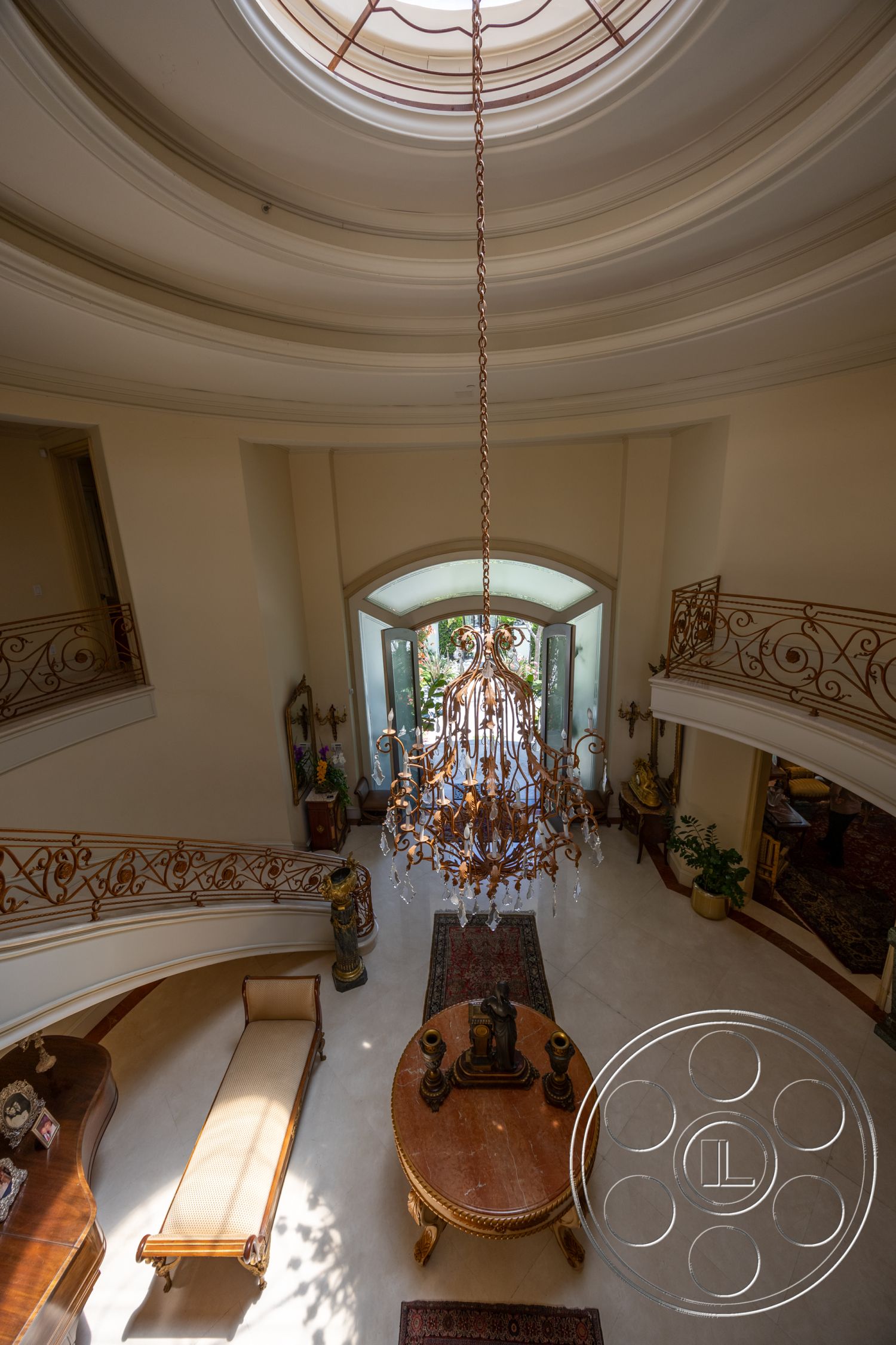Medit 165 - chandelier with crystal accents, curved staircase with wrought iron railing, interior grand foyer, vaulted ceiling with decorative molding, rounded skylight for natural lighting, marble flooring in entryway, traditional ornate wooden furniture, elegant area rug on marble floor, arched doorways leading to living area, decorative wall art and sculptures, potted greenery for indoor aesthetics, open layout design with natural light, high-end finishes and craftsmanship, neutral color palettes with warm tones, luxurious home entrance ambiance