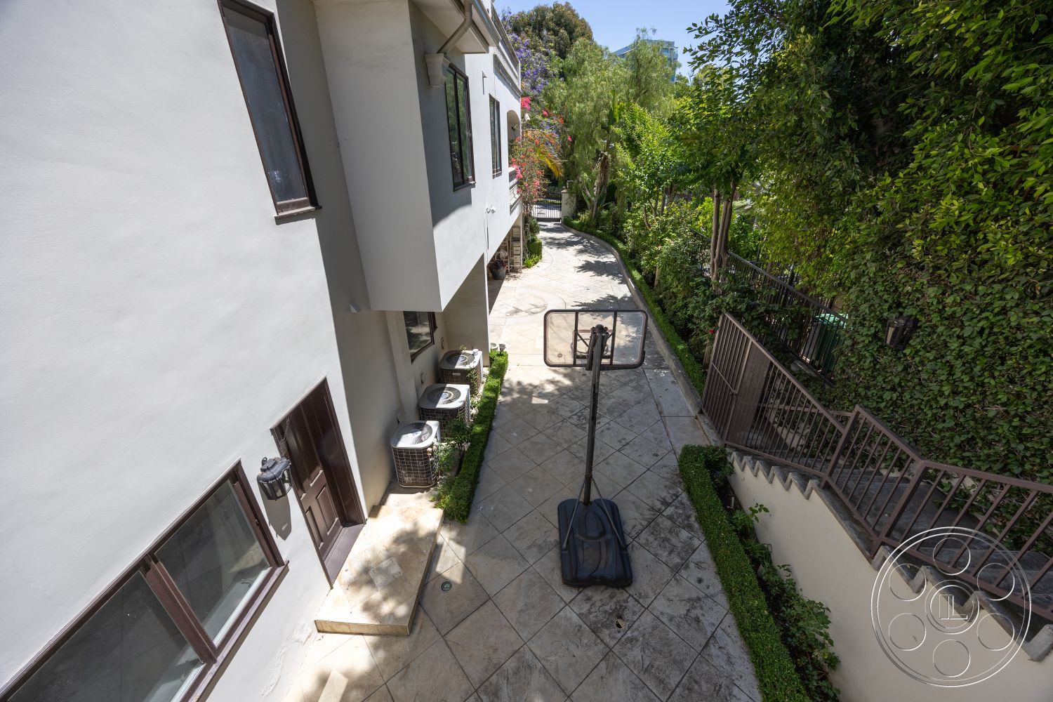 Medit 165 - modern light fixtures, concrete steps, contemporary architecture, green hedges, curved driveway, natural stone path, urban residential setting, outdoor living area, landscaped garden area, exterior stucco walls, metal railing details, gray painted exterior, slate tile driveway, basketball court area, basketball hoop installation, ground level access, pathway leading to home, framed windows with brown trim