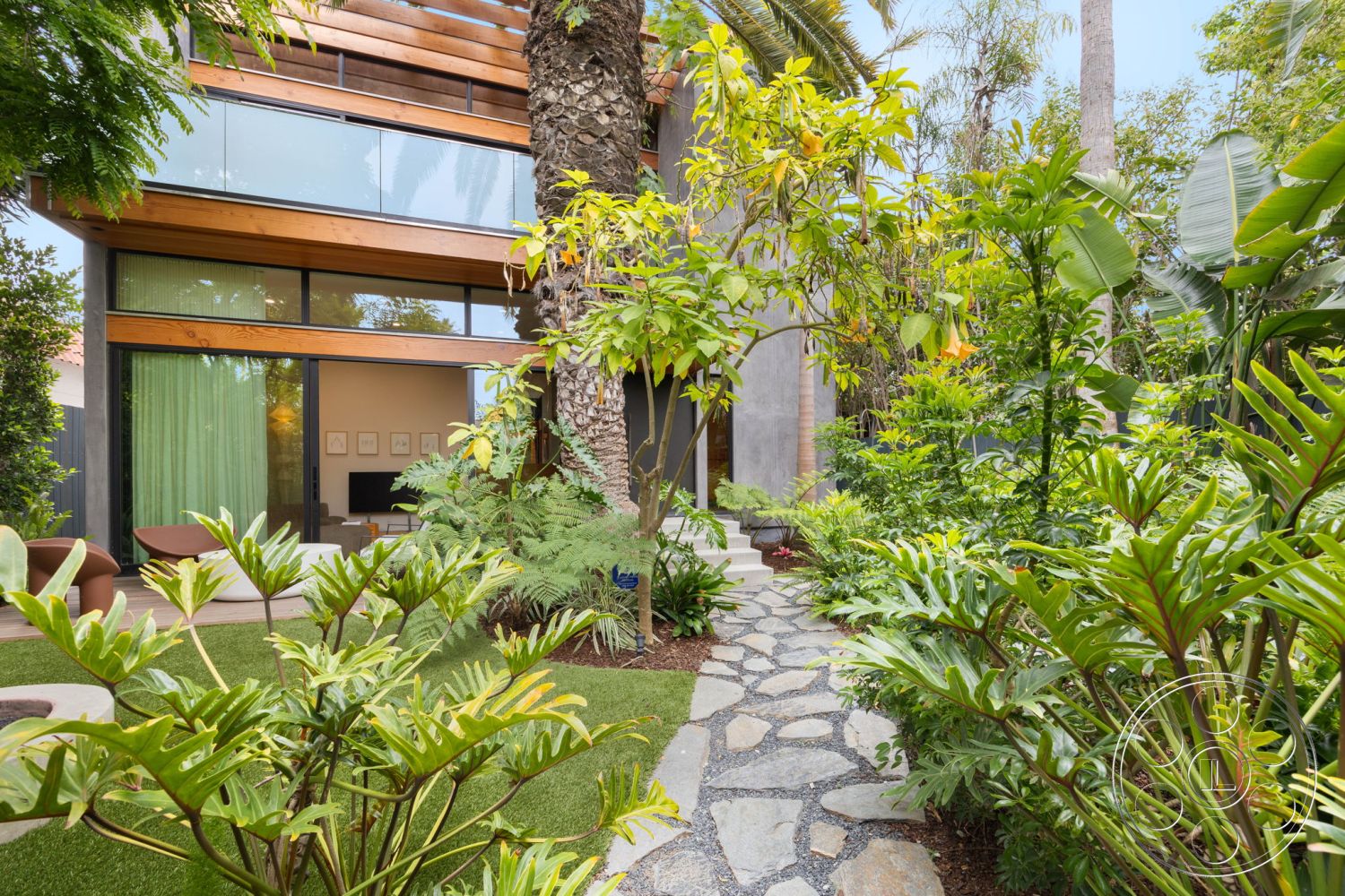Modern 508 - exterior, concrete pathway, stone stepping stones, modern architectural style, lush tropical landscaping, softscape features, garden seating area, wooden overhang, varied foliage, drought-resistant plants, contemporary home design, floor-to-ceiling glass windows, wooden deck patio, palm trees surrounding the space, green garden layout, natural stone detailing, multilevel outdoor environment, open living area with natural light, biophilic design elements