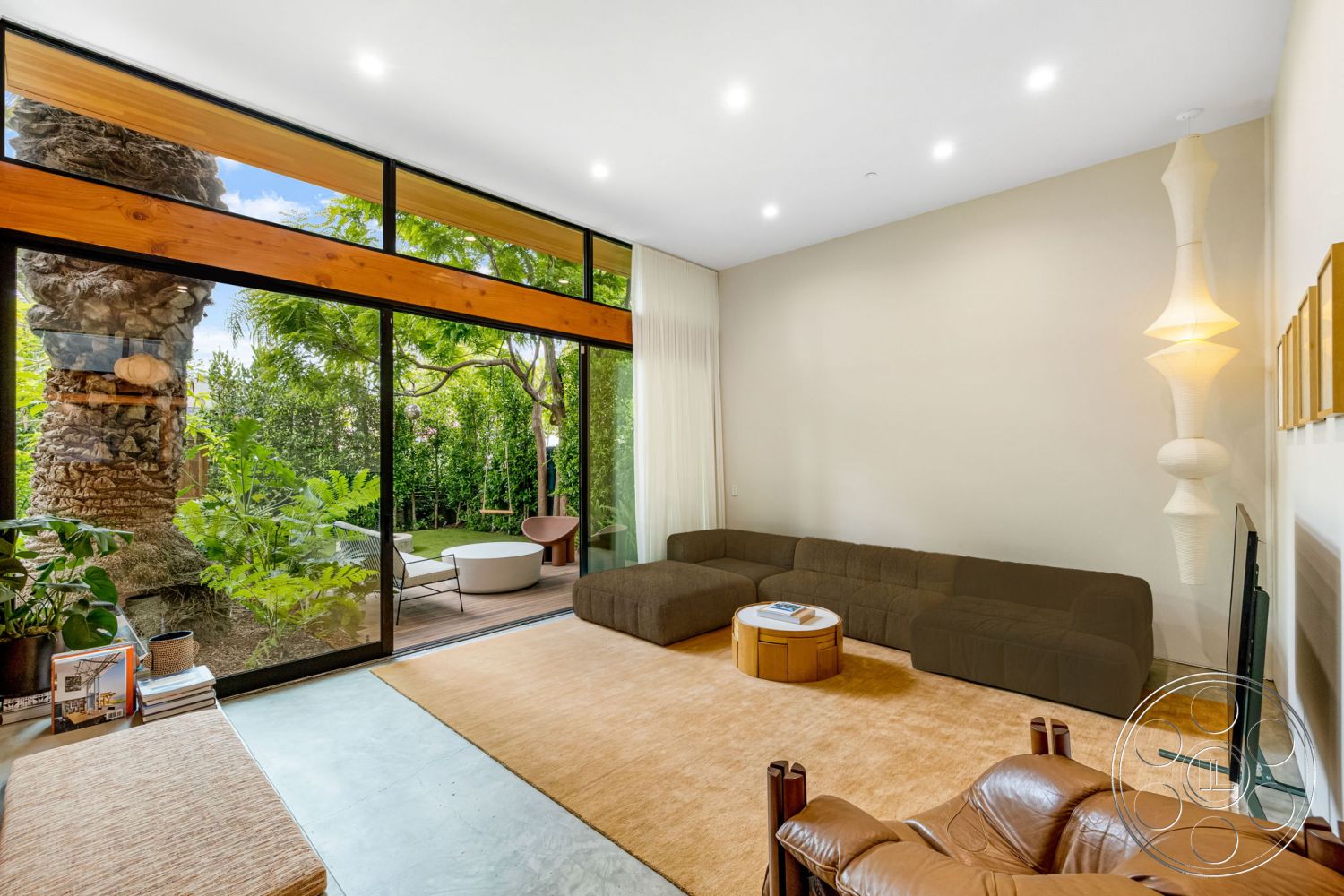 Modern 508 - floor-to-ceiling windows, textured plaster walls, round wooden coffee table, tan area rug, exposed wood ceiling beams, wood beam accents, mid-century modern design elements, modern sectional sofa, interior living room with concrete flooring, glass wall overlooking garden, large indoor potted plants, contemporary cushioned armchair, minimalist lighting fixture