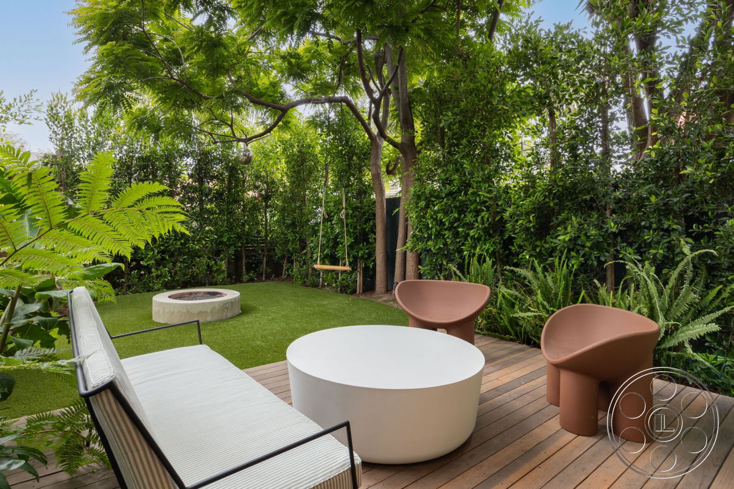 Modern 508 - wooden deck flooring, lush greenery surround, modern round coffee table, outdoor patio area, urban garden oasis, tropical landscape setting, contemporary molded chairs, lifelike artificial grass lawn, circular stone fire pit, private backyard retreat, decorative tree canopy, minimalistic outdoor furniture, swinging bench feature, interior outdoor space