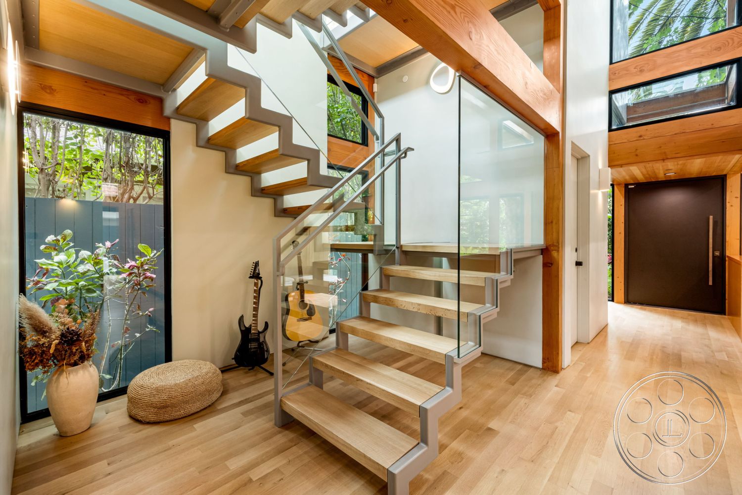 Modern 508 - open floor plan, indoor-outdoor flow, indoor greenery, large floor-to-ceiling windows, contemporary interior design, exposed wood ceiling beams, white painted walls interior, glass staircase railing, natural light entryway, floating wood stairs, hardwood flooring in foyer, modern front door design, potted plants as interior decor, minimalist stair design, structural wood elements