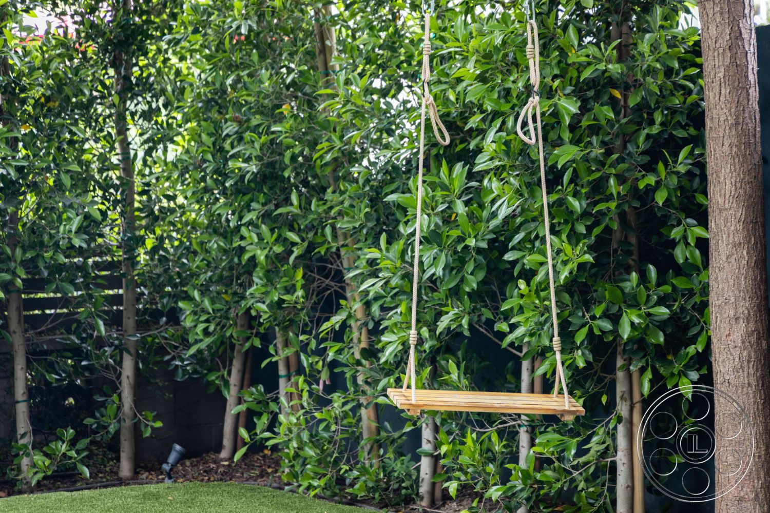 Modern 508 - natural wood materials, landscaped backyard, wooden swing, lush green foliage, peaceful outdoor retreat, exterior garden setting, soft grass lawn, natural rope swing, decorative privacy shrubs, sunny garden area, minimalistic outdoor design, casual garden seating, inviting play area