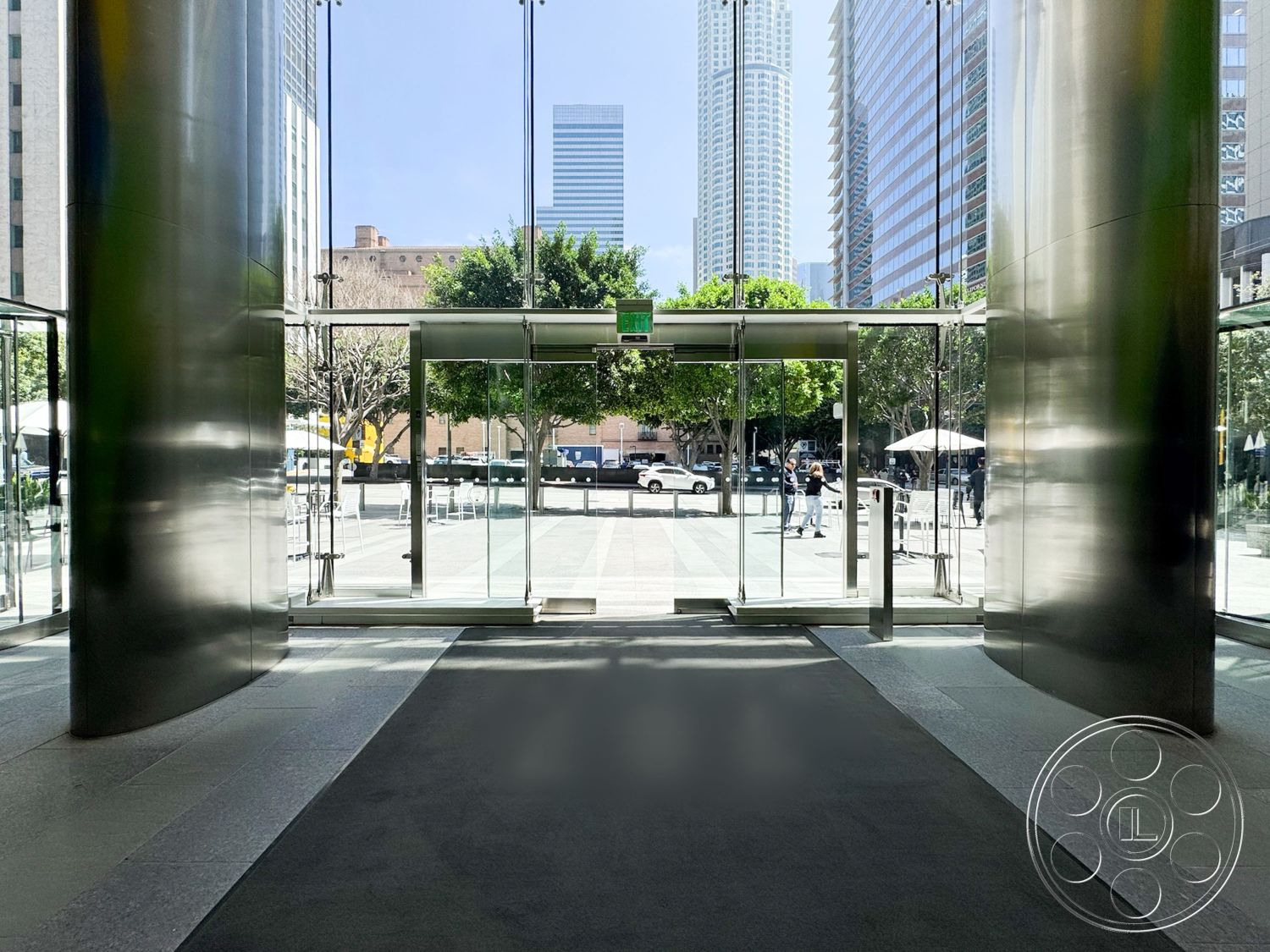 Office 122 - outdoor seating area, urban setting, landscaped courtyard, polished stone flooring, textured wall treatment, natural light interior, floor-to-ceiling glass windows, modern architectural design, commercial building entrance, exterior entryway, stainless steel columns, glass revolving doors, open plaza view, contemporary lobby space