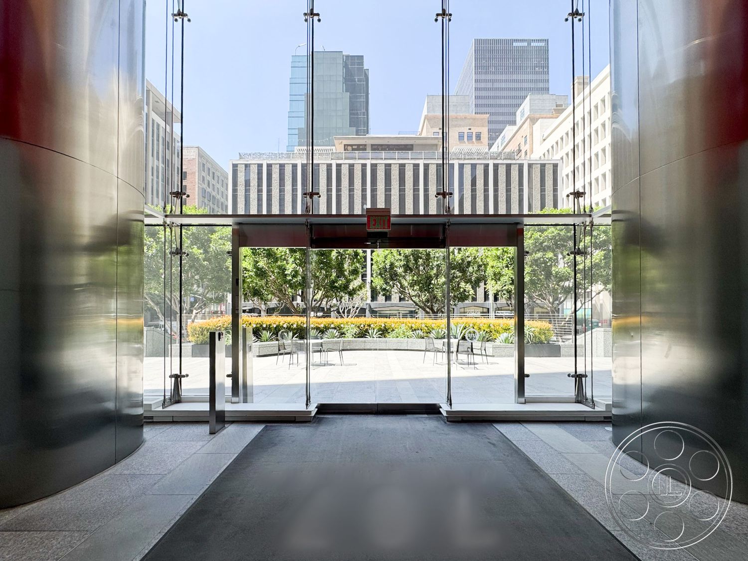 Office 122 - polished concrete flooring, floor-to-ceiling windows, city skyline view, contemporary architectural design, interior lobby space, exterior urban plaza, open air environment, glass facade entrance, steel framed glass doors, landscape with trees and seating, modern commercial setting, sleek metal wall treatment