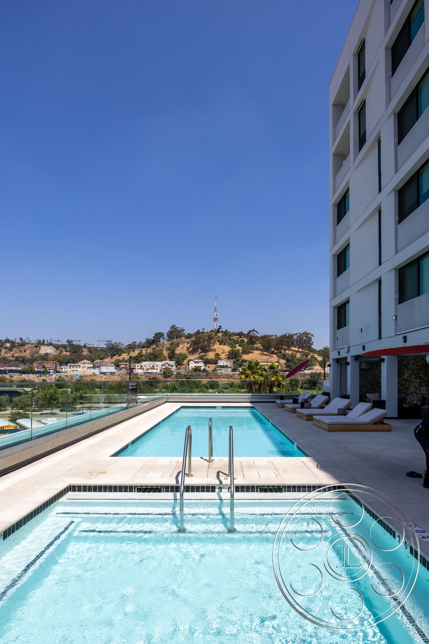 Apartment 55 - minimalist design elements, rectangular swimming pool, modern architectural style, exterior concrete pool border, exterior floor-to-ceiling windows, glass balcony railing, urban rooftop setting, sunny outdoor environment, exterior concrete patio flooring, lap pool design, exterior tile pool deck, landscape view with hills, exterior lounge chairs, contemporary swimming area, patio relaxation space