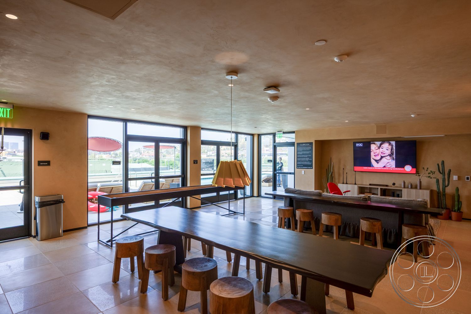 Apartment 55 - neutral color palette, modern decor, open concept layout, interior space, urban setting, minimalist furniture, textured plaster walls, rectangular dining table, television mounted on wall, acoustic ceiling tiles, pendant lighting fixture, natural light exposure, floor-to-ceiling glass windows, sealed concrete flooring, wood stool seating, potted cactus plants, multiple seating arrangements, commercial kitchen access, outdoor view from windows