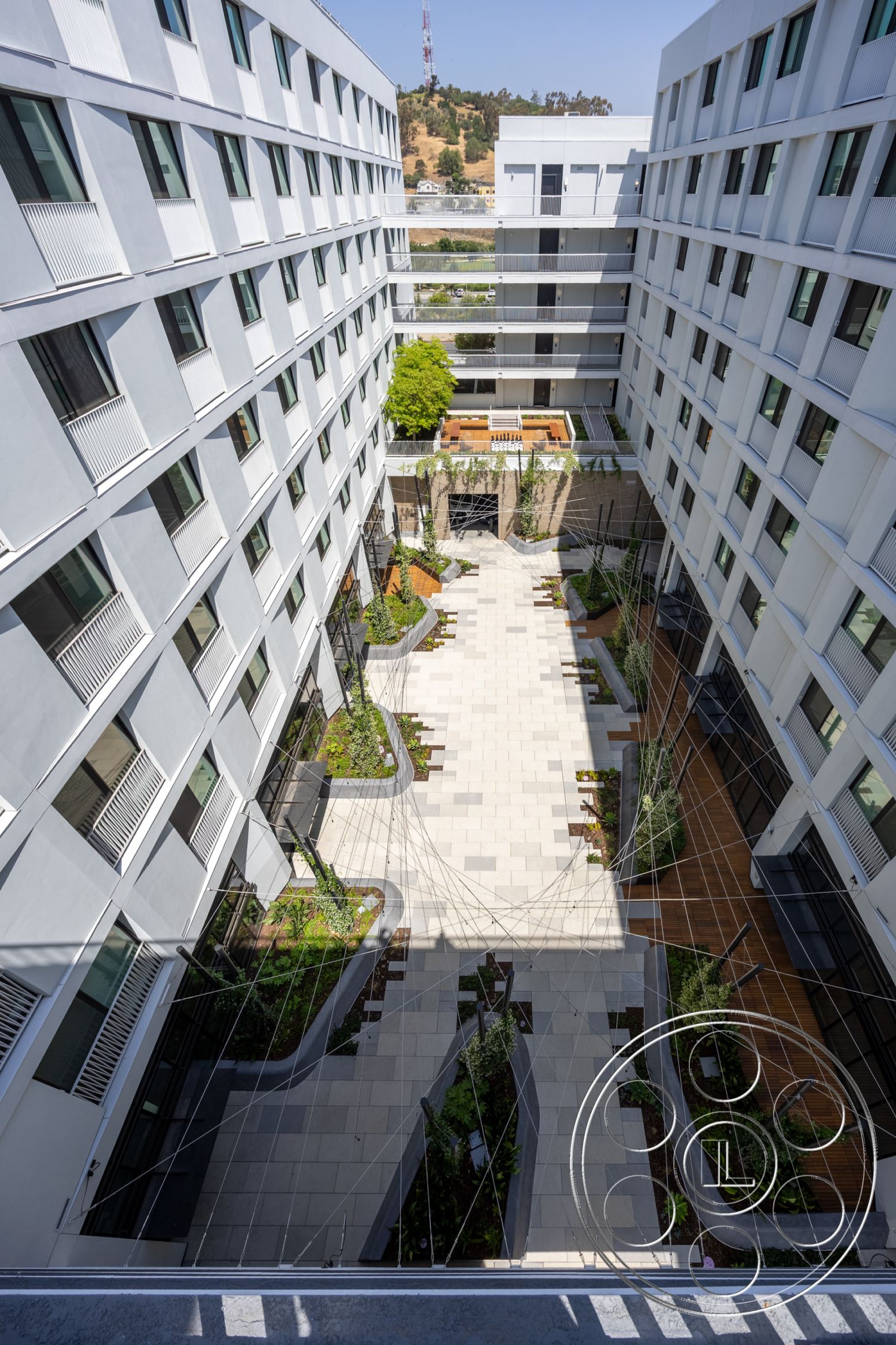 Apartment 55 - landscaped garden beds, minimalist architectural style, urban courtyard setting, steel railing details, concrete courtyard paving, modular concrete planters, rectangular outdoor seating area, flat roof building design, exterior glass curtain walls, horizontal louvered window screens, green space with low-maintenance plants, interior landscaped walkways, geometric patio layout, multiple story residential building, exposed electrical wiring features, open-air communal area, contemporary exterior façade