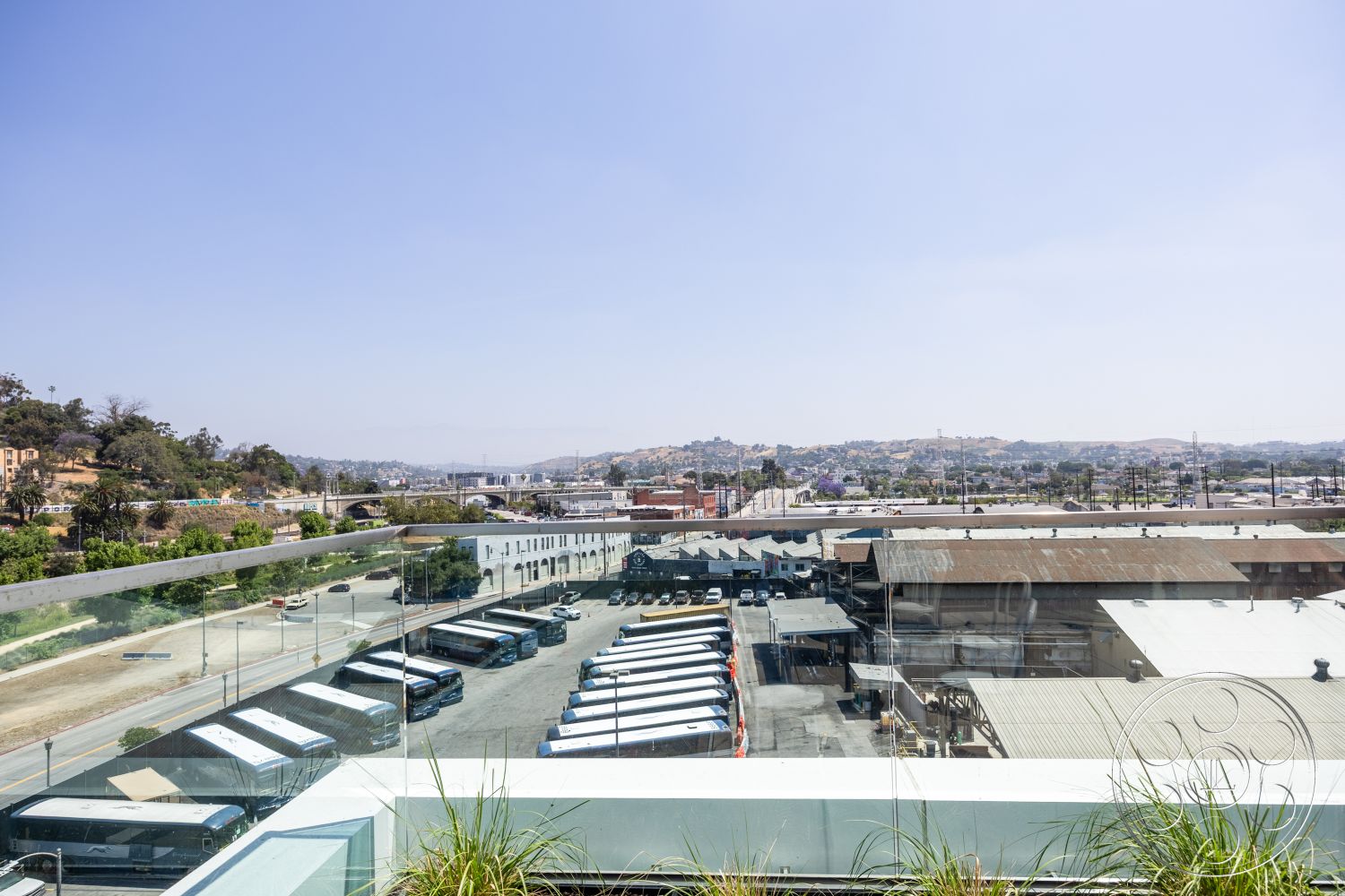 Apartment 55 - modern architecture, exterior view, urban setting, city skyline view, trees in background, commercial district, flat roof design, asphalt parking area, concrete balcony railing, glass balcony panels, landscaped rooftop garden, metal planter boxes, industrial buildings view