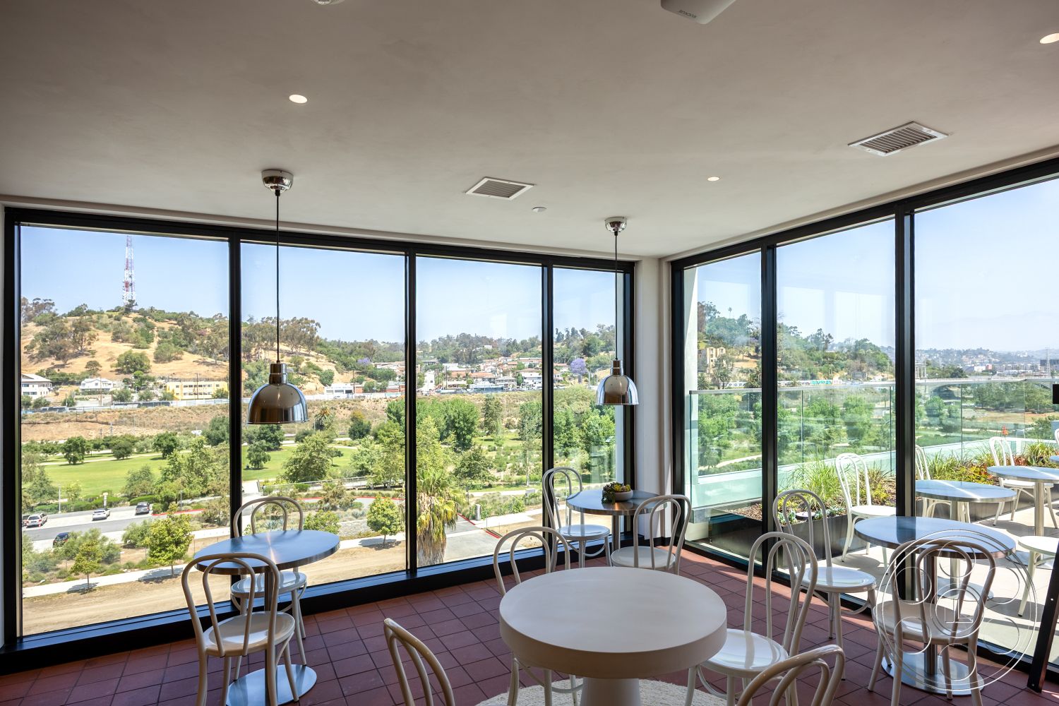 Apartment 55 - open floor plan, greenery visible through windows, modern dining chairs, minimalist room design, high ceiling with recessed lighting, natural light flooding space, contemporary interior decor, urban rooftop view, interior tile flooring, interior glass wall panels, hanging pendant light fixtures, round dining tables