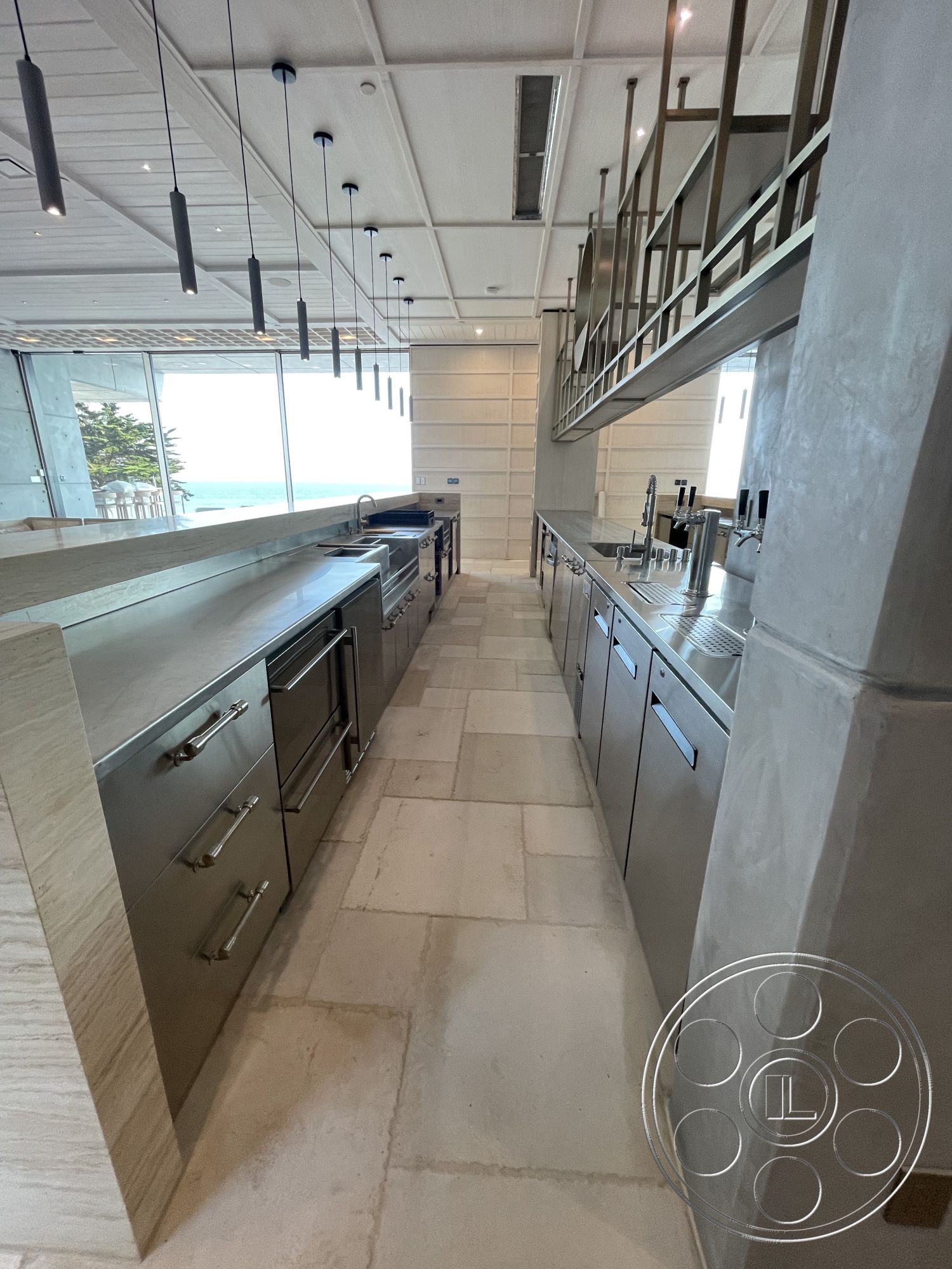 Modern 509 - natural light from large windows, concrete kitchen countertop, interior kitchen with stainless steel appliances, modern kitchen cabinetry with minimalist design, beachfront view kitchen, polished stone flooring in kitchen, sliding glass doors with ocean view, pendant lighting fixtures hanging from ceiling, open-plan kitchen layout, coffered ceiling with recessed lighting, full-height kitchen backsplash, integrated kitchen sink with seamless design, horizontal wood panel wall treatment, metal railing for upper level, kitchen island with additional seating, sophisticated kitchen design with clean lines