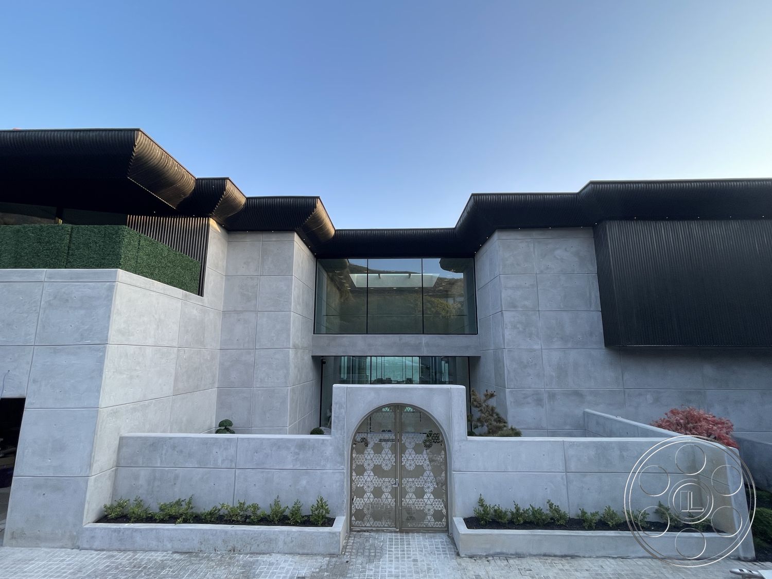 Modern 509 - minimalist design, floor-to-ceiling windows, modern architectural style, symmetrical facade, geometric forms, contemporary urban setting, flat roof design, exterior concrete walls, brick driveway pavers, rectangular building shape, exterior textured concrete facade, glass entryway, arched entrance gate, horizontal wood slat details, landscaped patio area, green border landscaping, light-colored stone accents, steel accent features, open space entry, shaded outdoor areas