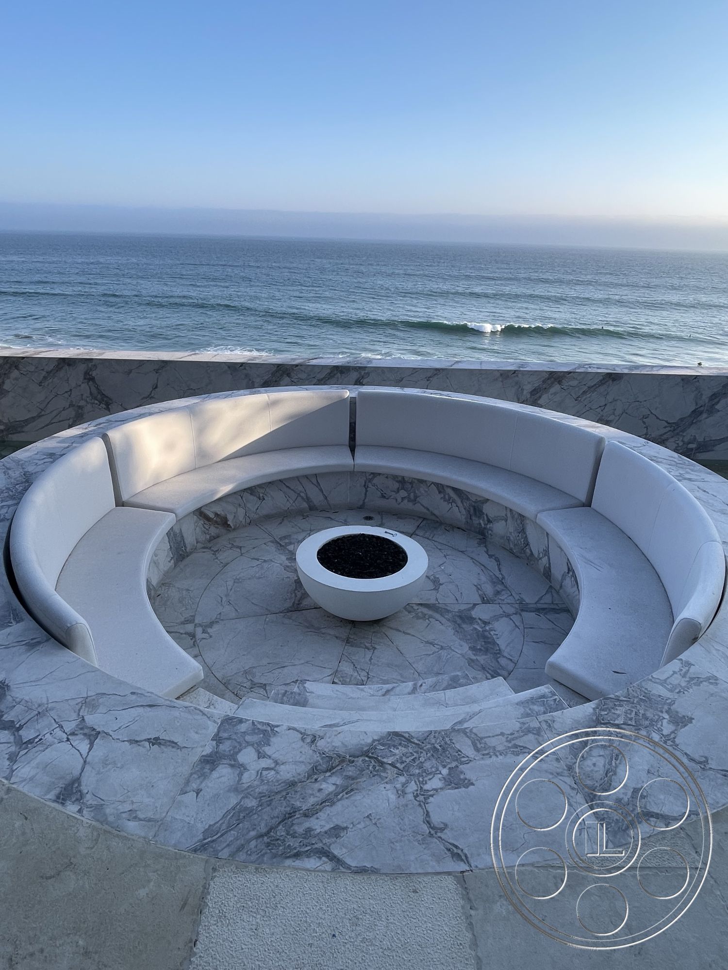 Modern 509 - minimalist design elements, modern outdoor furniture, relaxation area, outdoor entertainment space, white stone accents, concrete fire pit, curved sectional seating, marble seating wall, circular outdoor lounge area, textured stone patio surface, coastal beachfront setting, sea view backdrop, smooth marble flooring, exterior fire feature, high-end outdoor living, sunset horizon, oceanfront terrace, luxury outdoor oasis, interior or exterior