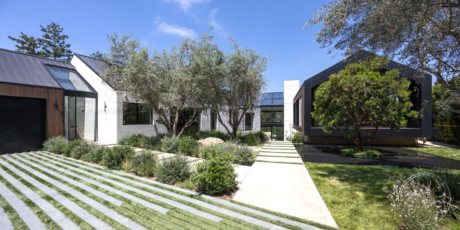 Modern 510 - exterior concrete driveway, exterior stone pathway, exterior stone wall cladding, exterior grass strip landscaping, wood paneling garage door, glass entryway doors, modern style roof design, rectangular lawn, exterior flat roof, exterior trees and shrubs landscaping, eclectic architectural style blending, minimalist front yard design, contemporary single-story house, exterior aluminum window frames, neutral color scheme on walls, symmetrical home layout, sloped yard design, exterior concrete slab walkway