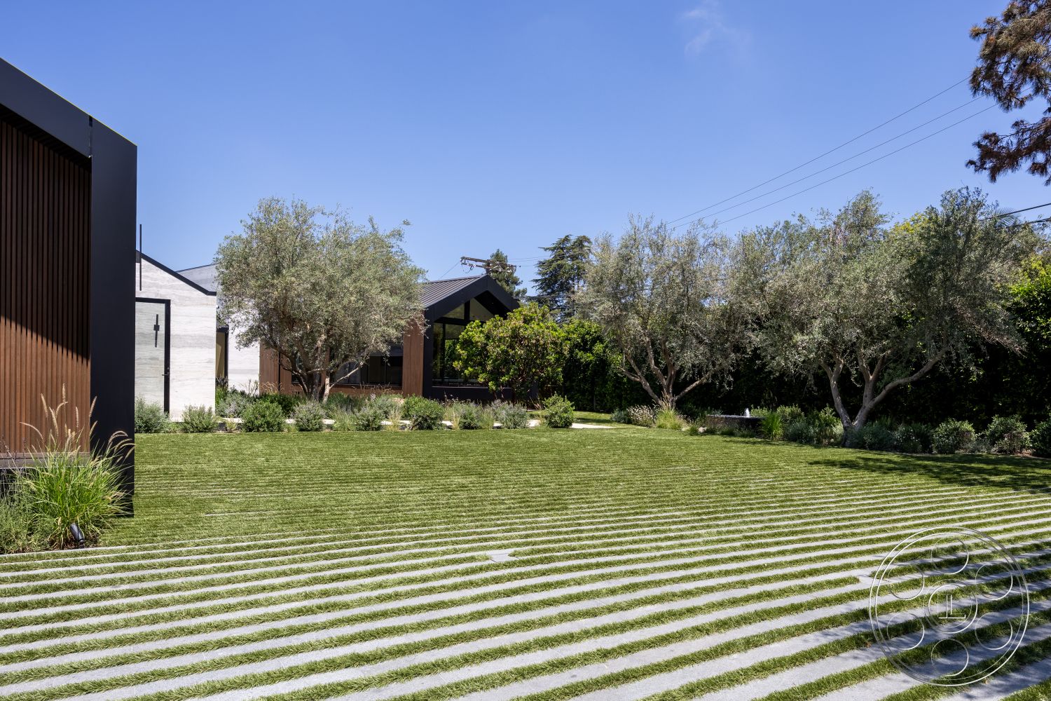 Modern 510 - front yard, large glass windows, suburban backyard, stone planters, functional outdoor area, open green space, modern ranch-style home, minimalist architectural style, striped grass lawn, exterior landscape design, concrete pathway with grass inlays, modern rectangular home, wood panel exterior cladding, decorative shrubbery landscaping, olive trees in garden setting