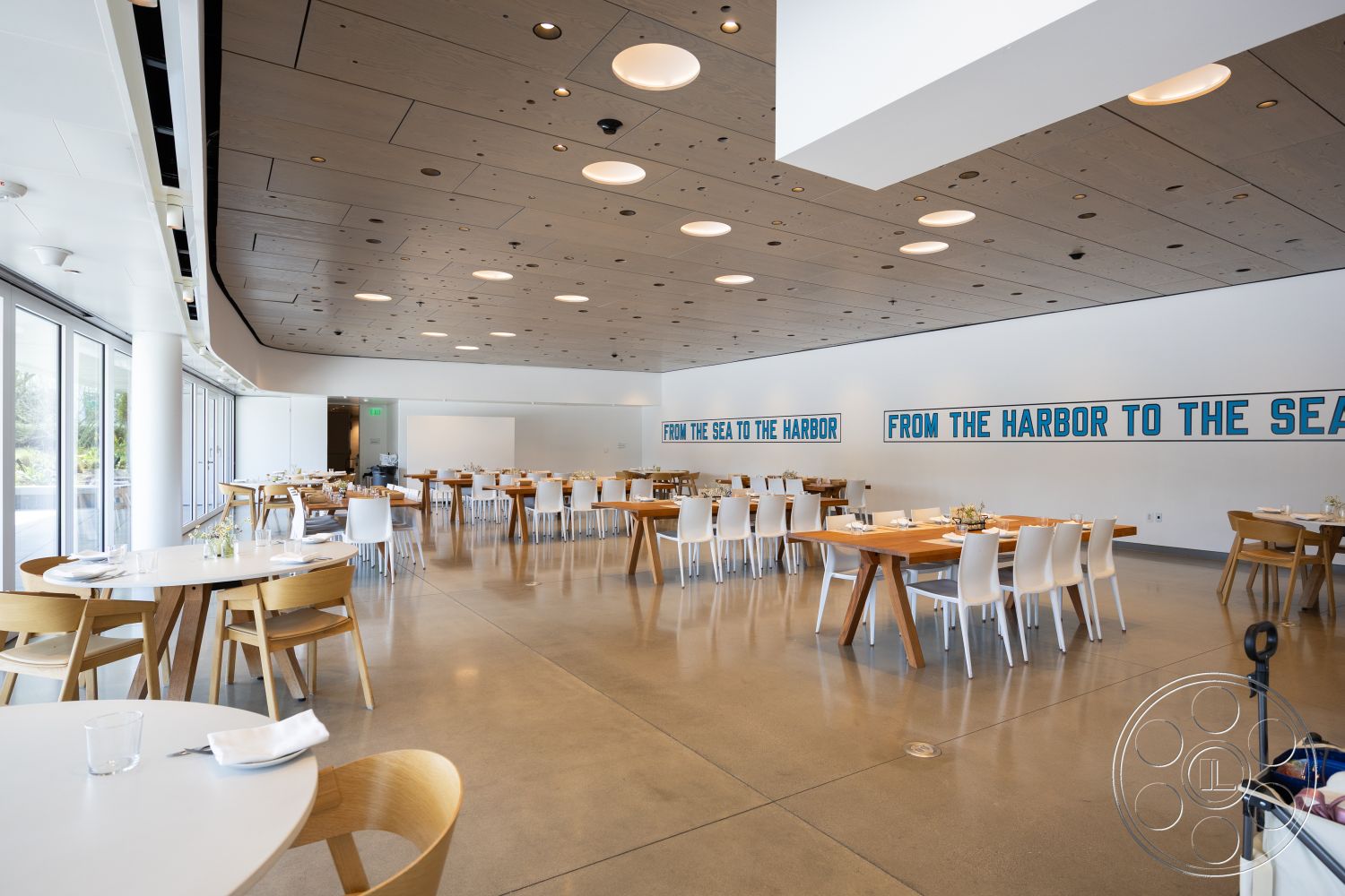 Museum 4 - neutral color palette, modern light fixtures, minimalist design elements, floor-to-ceiling windows, textured wall panels, exposed concrete ceiling, spacious dining area, clean lines architecture, open layout space, ambient lighting design, wall-mounted signage, interior concrete floor, light wood dining tables, simple white dining chairs, round dining table arrangement, urban restaurant setting, seaside view ambiance