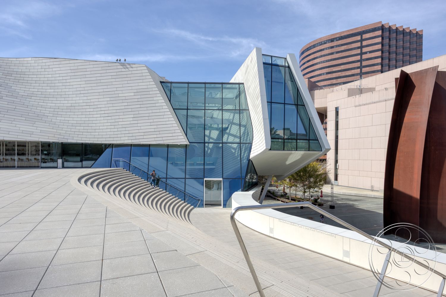 Museum 4 - exterior, outdoor gathering space, modernist design, surrounding urban environment, angular architectural forms, glazed steel curtain wall, metal roof cladding, concrete steps with curved edges, landscaped plaza setting, organic shapes in architecture, panoramic glass windows, complementary metal accents, stylized exterior staircases, sculptural facade elements