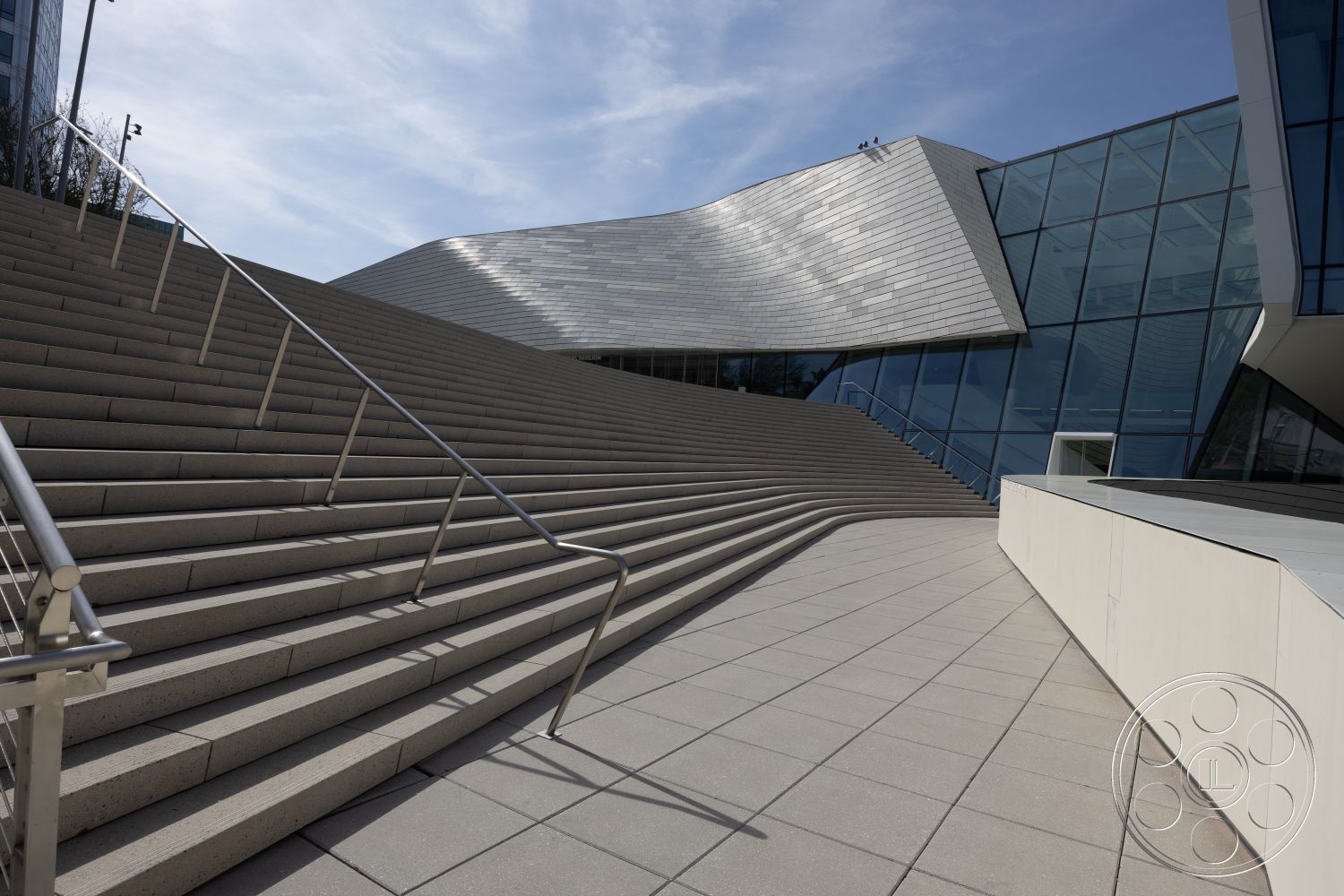 Museum 4 - innovative design elements, natural light exposure, modern building design, integrated landscaping features, open urban setting, exterior concrete staircase, gray concrete steps, stainless steel stair railings, large glass facade, slate roof design, smooth concrete patio flooring, angular architectural shape, string of exterior ambient lighting, geometric forms in architecture, curved exterior wall, clean minimalist lines
