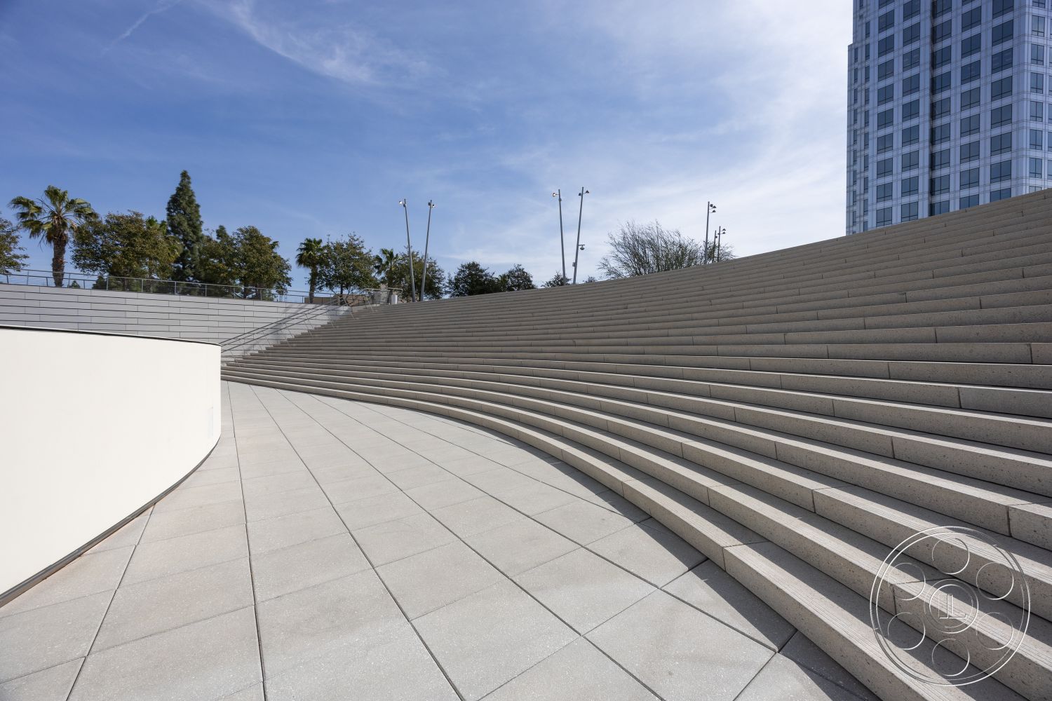 Museum 4 - polished concrete flooring, outdoor gathering space, textured concrete wall, smooth concrete finish, integrated lighting fixtures, modern architectural design, urban setting with high-rise buildings, curved concrete steps, exterior concrete amphitheater seating, landscaped surrounding area with palm trees