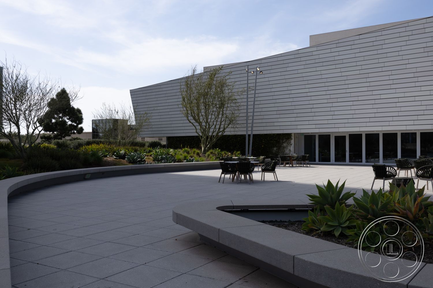 Museum 4 - urban setting, glass windows, outdoor dining area, modern landscape design, contemporary architectural style, exterior patio flooring, steel outdoor furniture, smooth concrete tiles, curved concrete seating area, low-maintenance succulent garden, rectilinear building facade, light-colored metal wall cladding, symmetrical plant arrangement, sculpted landscaping