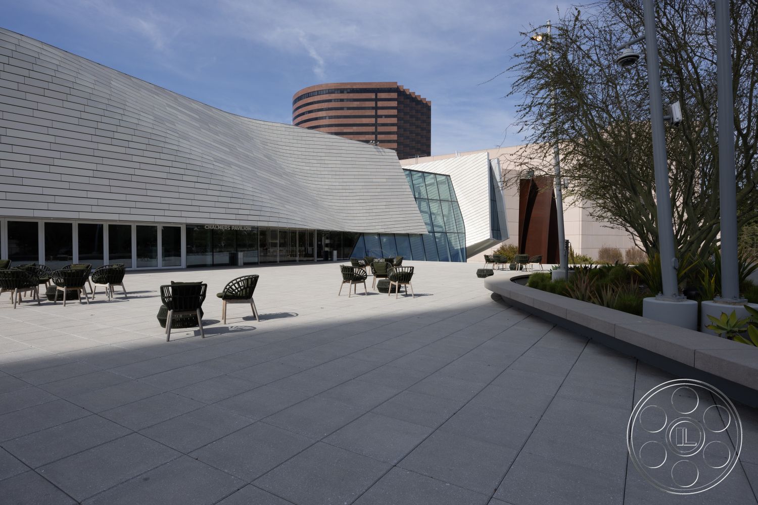 Museum 4 - outdoor seating area, textured wall panels, urban environment, lounge chairs, city skyline view, concrete walkway, interior patio floor tiles, glass entrance facade, curved architectural roof design, metal siding exterior, linear planter beds, exposed structural steel elements, modernist design details, landscaped exterior space