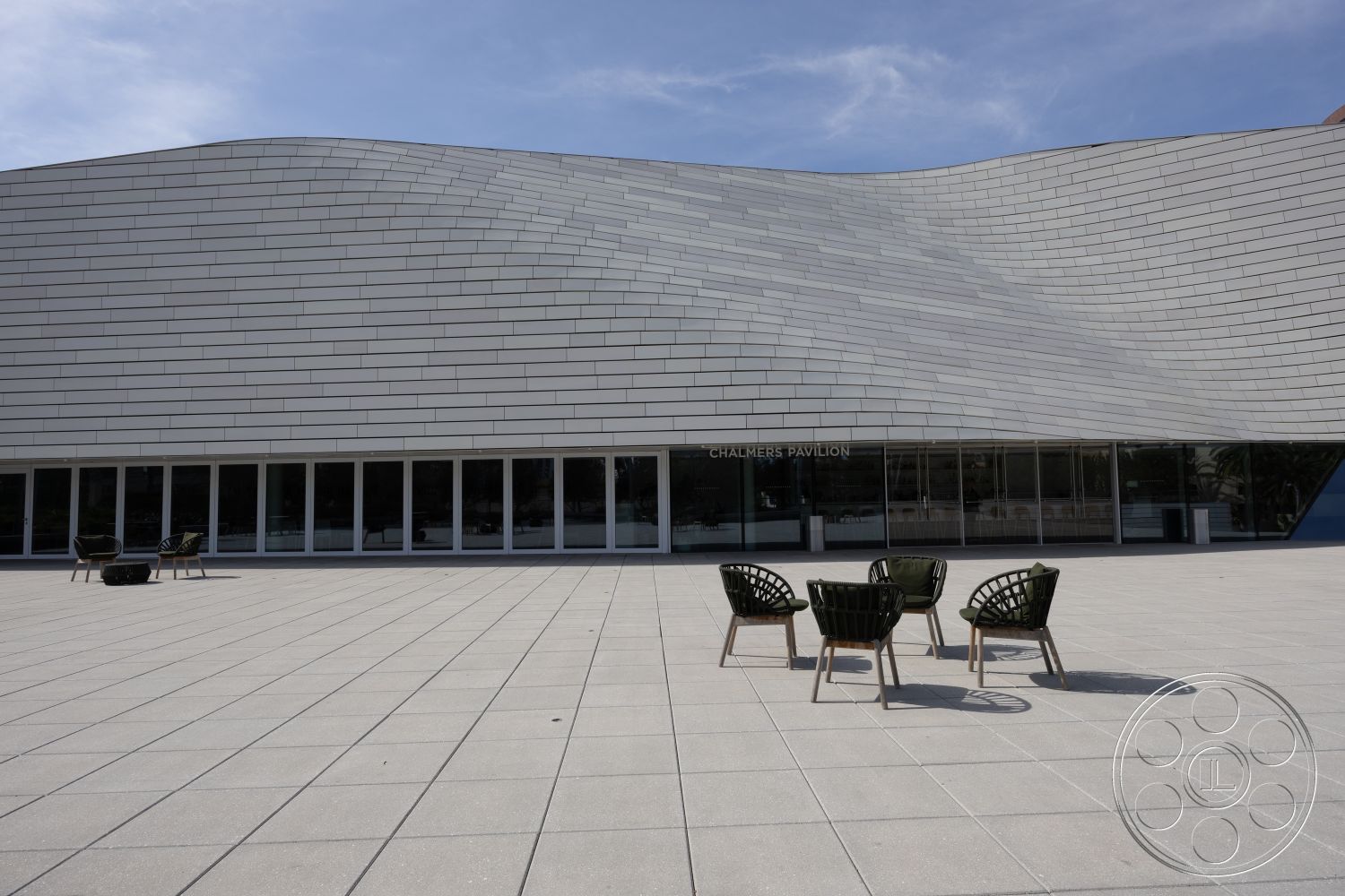 Museum 4 - open space for gatherings, modern outdoor seating area, sleek contemporary design, concrete outdoor patio flooring, exterior facade with textured white metal panels, curved architectural form, large glass windows for natural light, functional exterior layout, minimalist aesthetic with surrounding urban environment