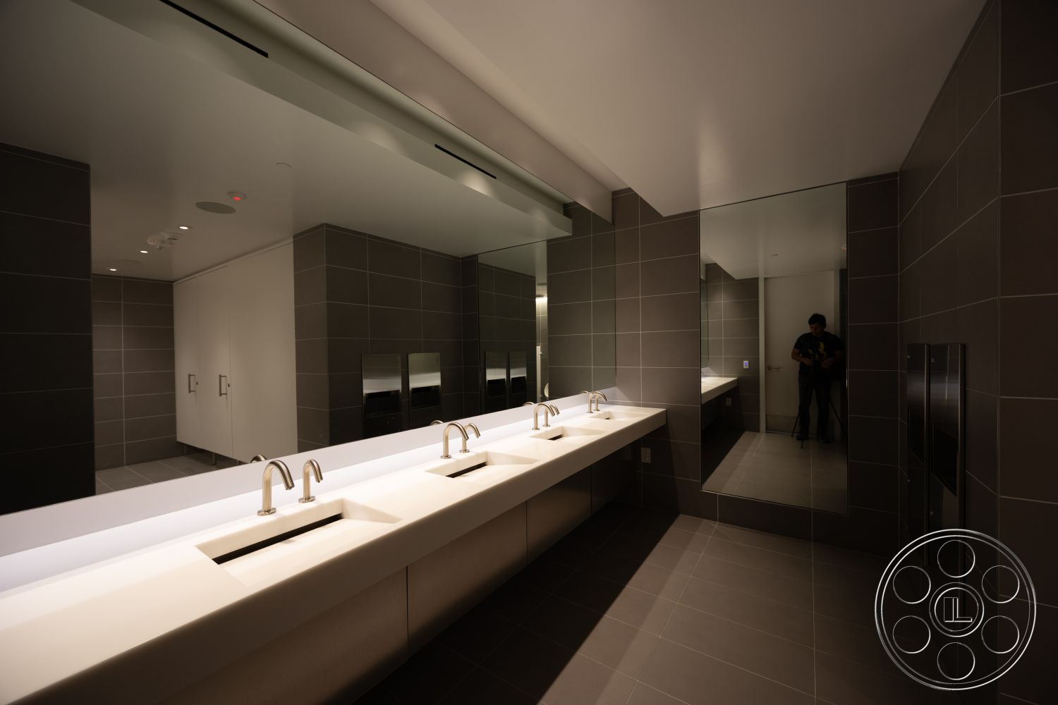 Museum 4 - neutral color palette, minimalist design, concrete countertop, polished tile flooring, white painted walls, modern faucet fixtures, tile bathroom walls, ambient ceiling lighting, rectangular sinks, glass mirror wall, exterior restroom setting, accessible bathroom design, commercial bathroom space, floor-to-ceiling mirrors, user-friendly fixtures