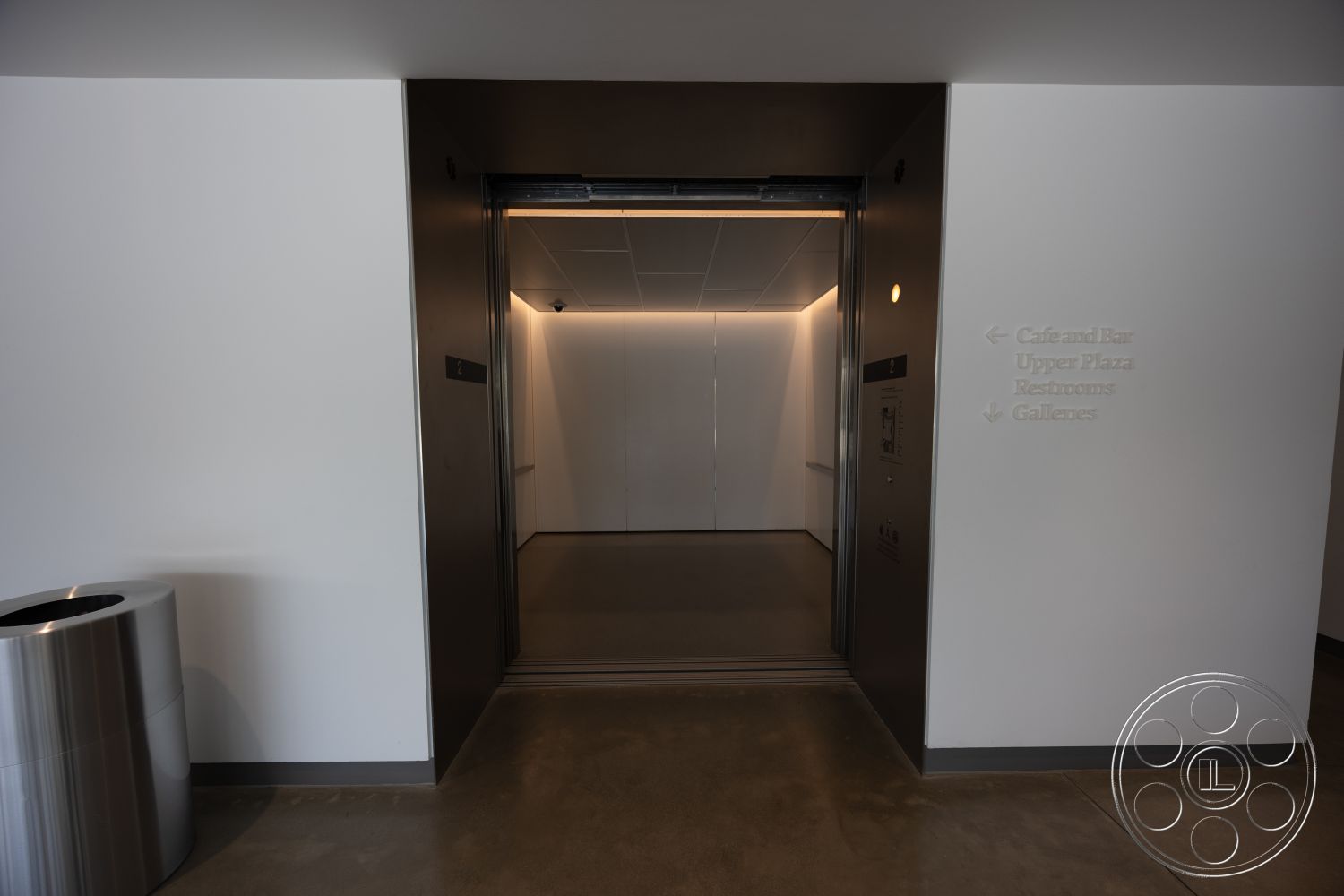 Museum 4 - modern minimalist aesthetic, concrete floor finish, LED recessed lighting, commercial building interior, stainless steel elevator doors, interior elevator entrance, flushed white drywall, signage wall with directional text, clean lines architectural style, crisp geometric shapes