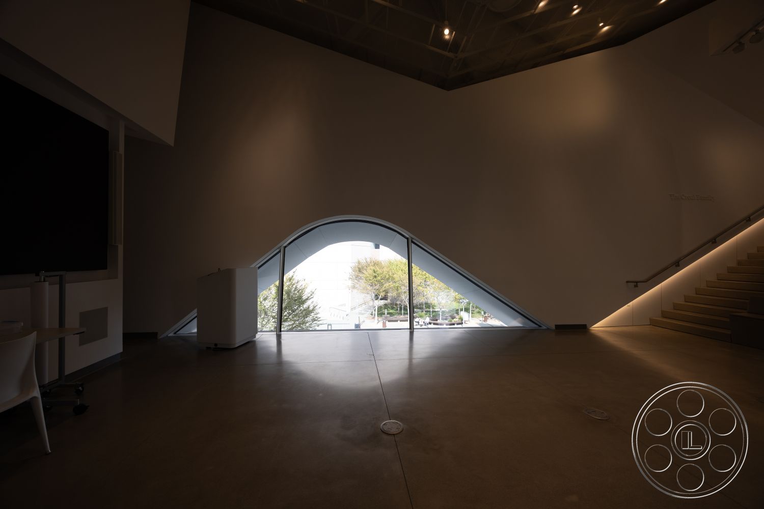 Museum 4 - neutral color palette, minimalist aesthetic, open floor plan, multifunctional space, exposed ceiling structure, textured plaster wall finish, natural light emphasis, contemporary architectural design, steel stair railings, interior concrete floors, curved glass windows, angular wall shape, modern wall treatment, focal point window, geometric interior elements, urban setting view, landscape framing, multi-dimensional surfaces