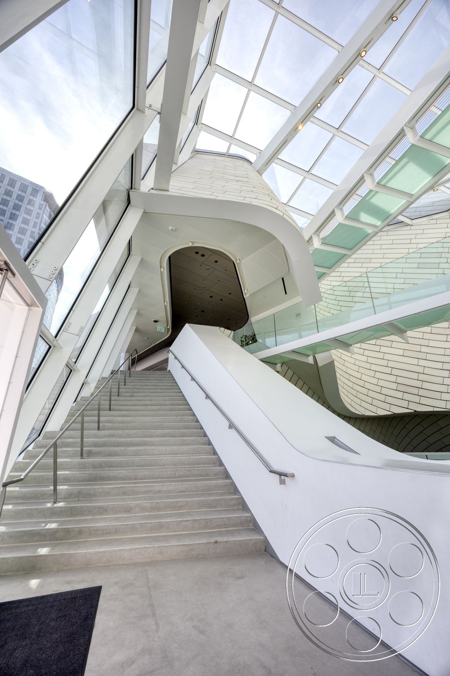 Museum 4 - minimalist design elements, glass railing, natural light from skylights, curved architectural forms, textured ceiling panels, interior concrete staircase, modern white walls, skyline view through glass walls, open stairwell, innovative structural elements