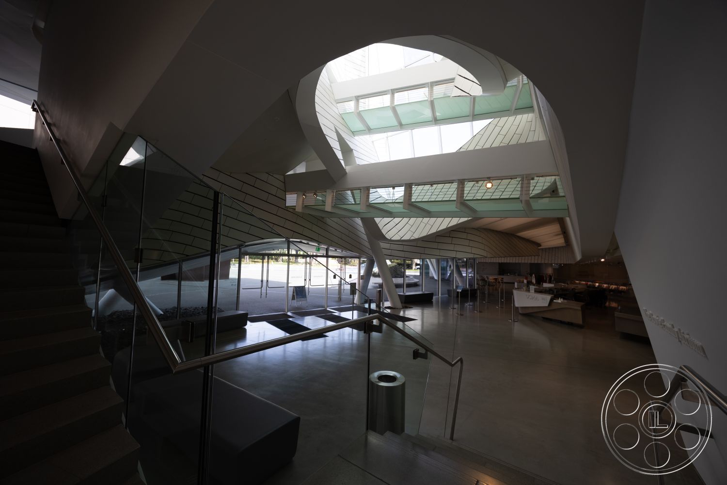 Museum 4 - neutral color palette, floor-to-ceiling windows, open-plan layout, glass partition walls, modern minimalist design, natural light-filled space, urban contemporary aesthetic, interior concrete floor, polished concrete steps, exposed steel structural elements, vaulted ceiling with wood accents, curved architectural shapes, low-profile furniture arrangement, angular ceiling lines, sculptural stair design
