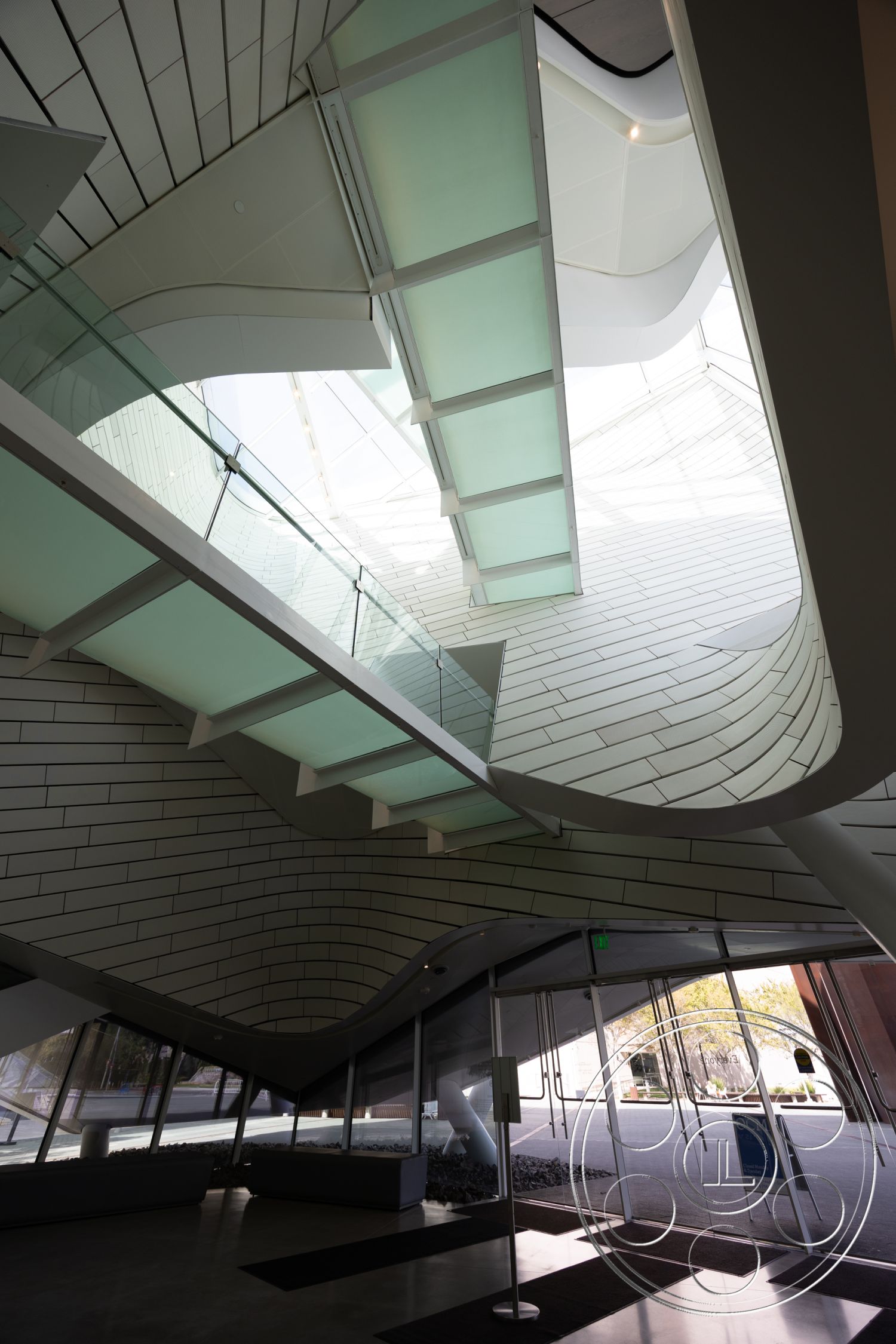 Museum 4 - textured wall panels, exposed concrete floor, white plaster walls, integrated lighting fixtures, floor-to-ceiling glass windows, minimalist architectural style, curved ceiling design, contemporary lobby space, modern metal railings, interior glass staircase, geometric glass skylight, smooth composite wall surface, elevated walkway with glass panels, open-concept entryway, angular structural elements