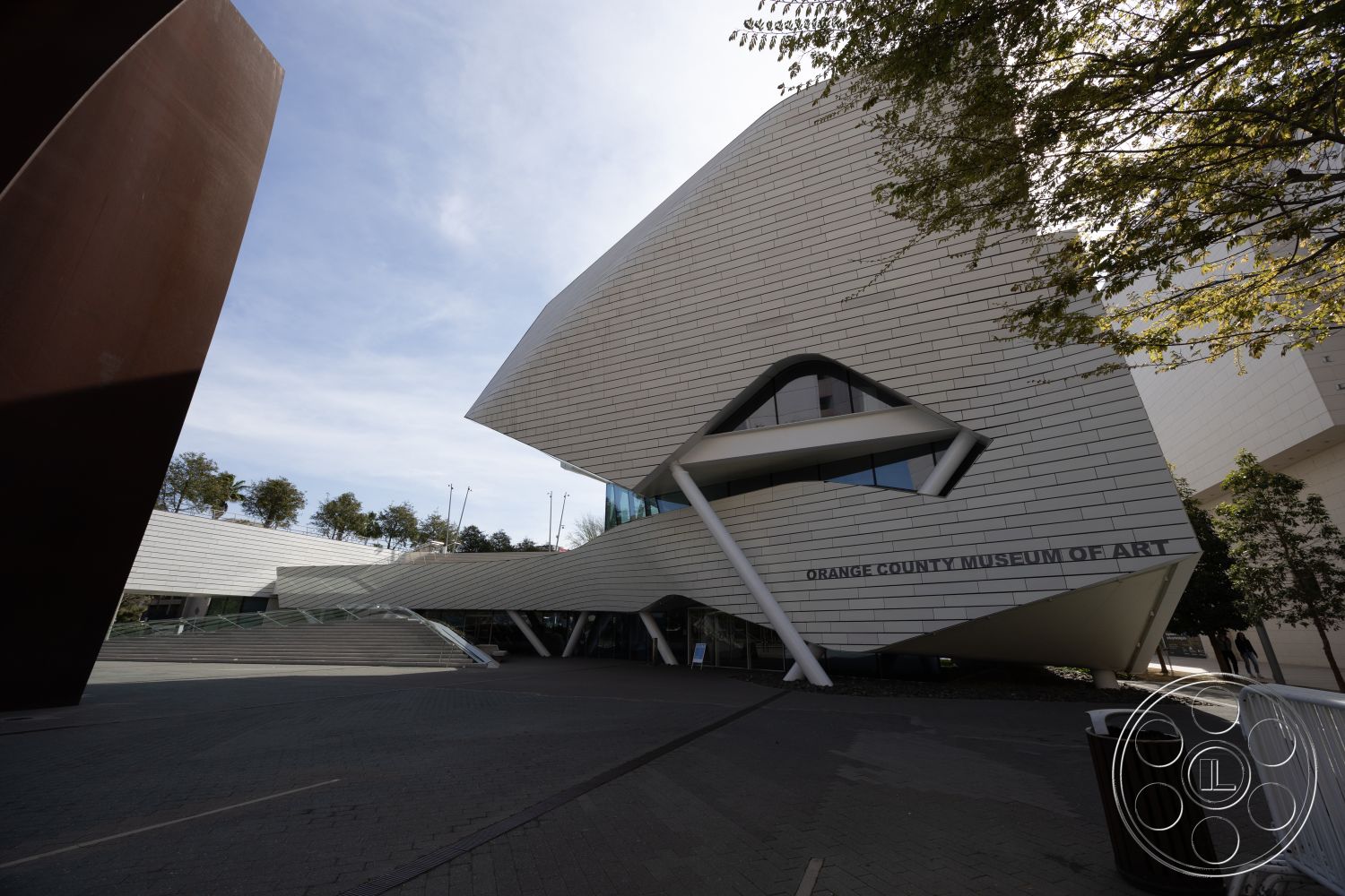 Museum 4 - exterior, large glass windows, concrete pathway, contemporary architecture, metal panel facade, angular architectural shapes, asymmetrical building design, landscaped entrance area, stepped terrace, modern art museum, urban art space, sculptural external elements, surrounding tree line, open outdoor plaza, interplay of light and shadow, exposed structural supports