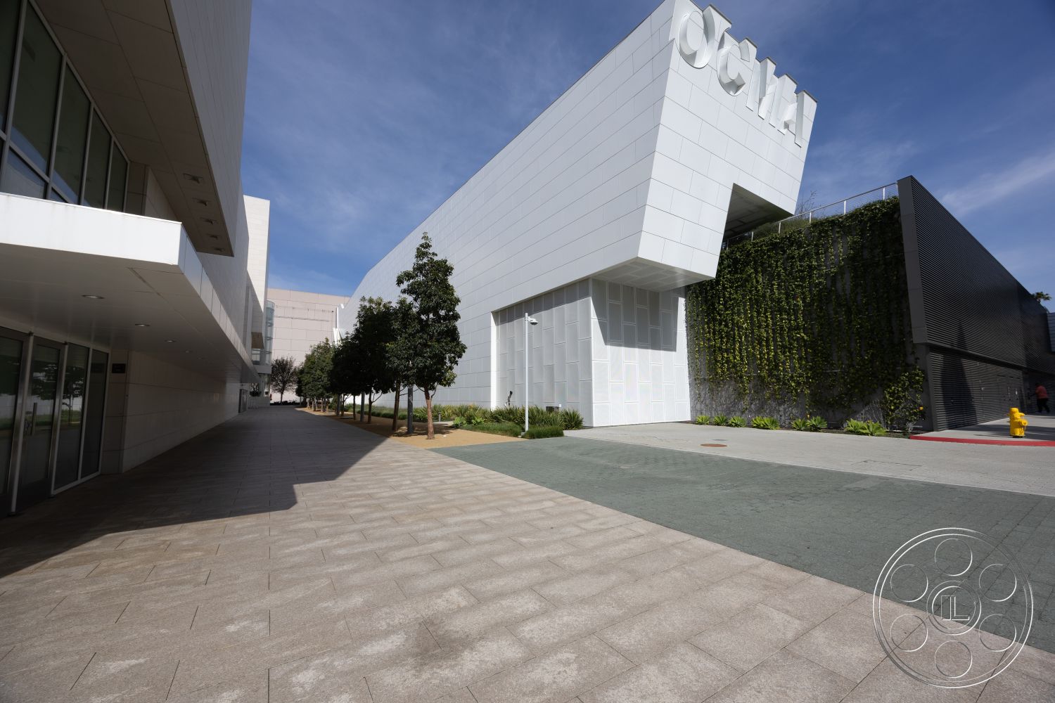Museum 4 - exterior, modern architecture, minimalist design, large glass windows, curved pathway, planted greenery, green living wall, landscaped garden area, concrete paver walkway, urban plaza setting, rectangular building shape, white cladding exterior walls, vertical garden detail