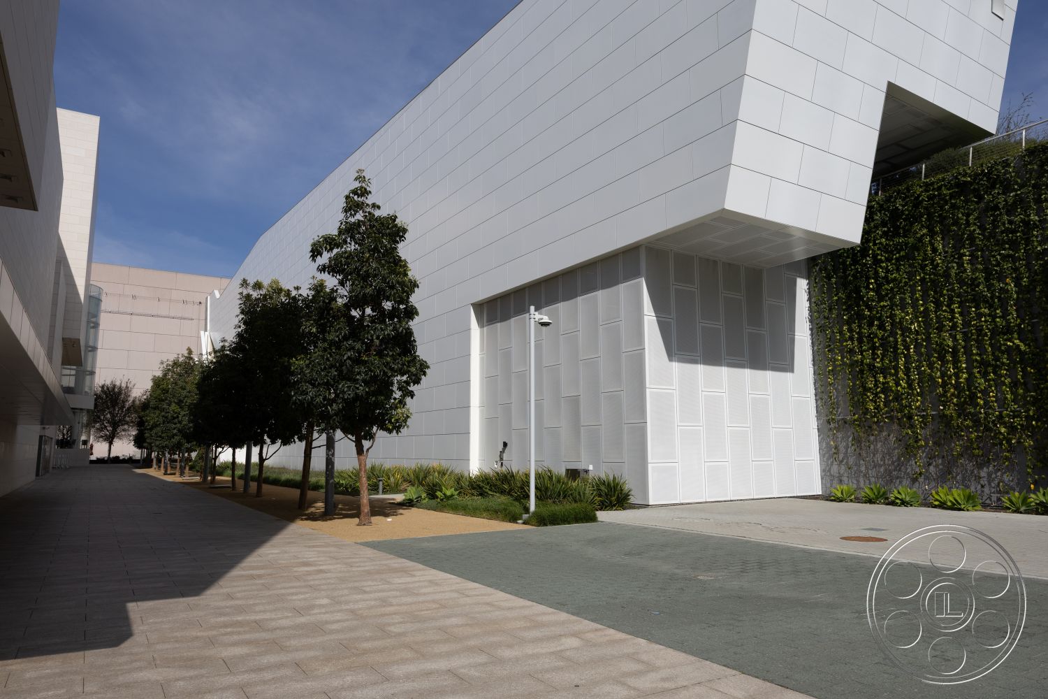 Museum 4 - exterior, minimalist design elements, modern architectural style, concrete walkway, sustainable landscaping, natural light ambiance, textured concrete pavers, clean lines and angles, white panel facade, landscaped pathway with trees, rough-textured stone wall, green vine-covered wall, planted greenery for shade, sidewalk with geometric patterns, elevated building structure