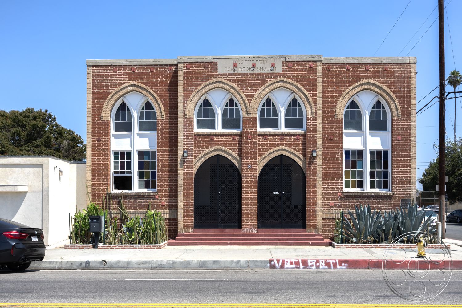 Studio 100 - high ceilings, arched windows, church, concrete steps, historic building, commercial building, two-story structure, concrete sidewalk, landscaped front garden, glass window panes, exterior brick facade, urban street setting, red brick building, gothic architectural details, stone window trim, entrance with double doors, decorative cornice molding, symmetrical facade design, front entrance stairs, plantings along the base