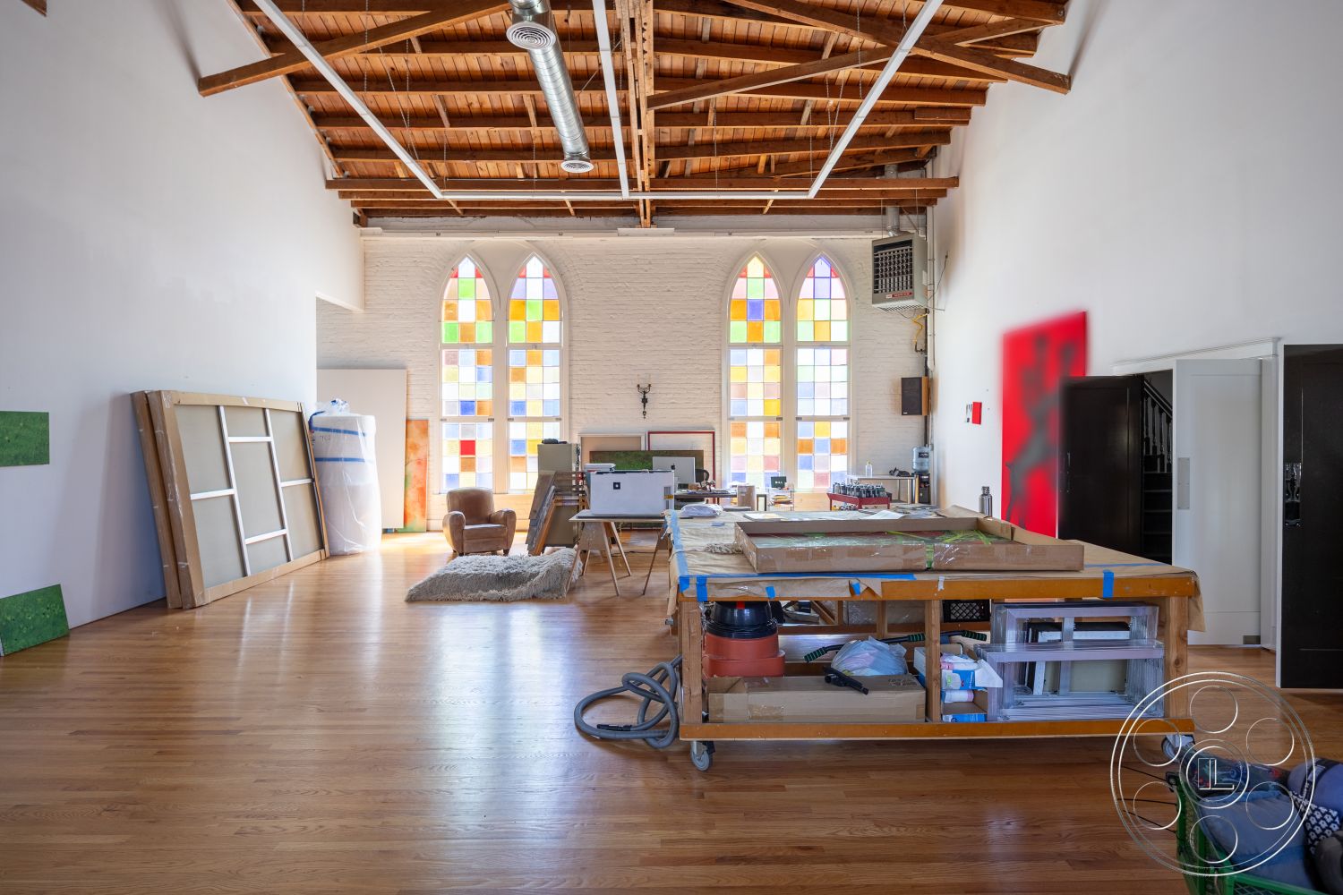 Studio 100 - open floor plan, natural wood accents, artistic workspace, creative environment, stained glass windows, textured plaster wall, hardwood floor interior, exposed wood beam ceiling, natural light flooding interior, modern industrial aesthetic, open concept studio space, interior painting station, wooden work table, historic building repurposing, functionality with aesthetic appeal