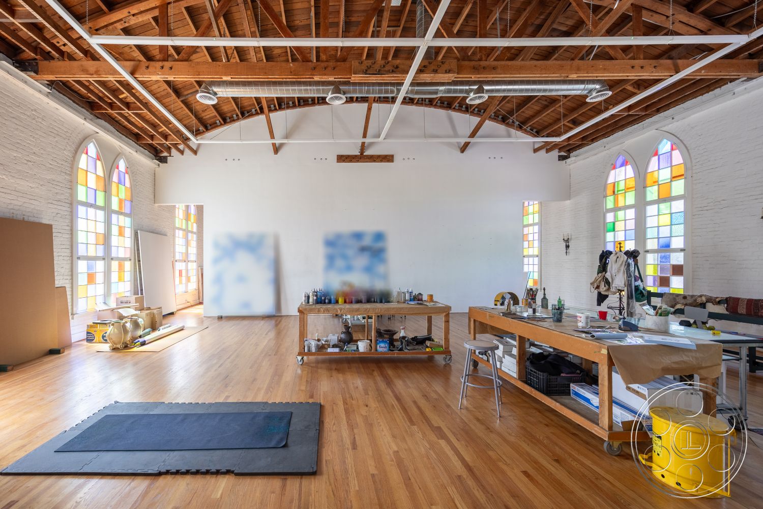 Studio 100 - minimalist design, inviting atmosphere, artistic workspace, stained glass windows, exposed wood ceiling beams, natural light interior, white painted walls, open floor plan interior, exposed brick accent wall, creative studio environment, hardwood studio floors, industrial ceiling fixtures, large studio space, organic materials usage, functional work table, workspace with storage, flexible room arrangement, colorful window details, urban loft style